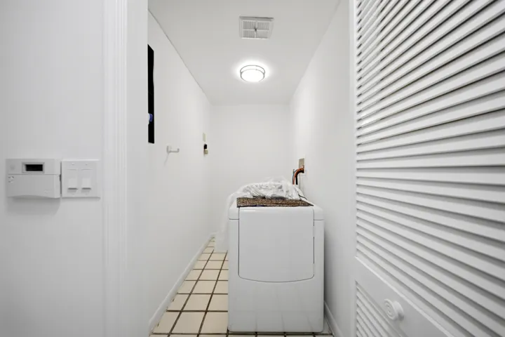 Dedicated laundry area featuring tile flooring, white walls, louvered bi-fold doors, and recessed ceiling lighting