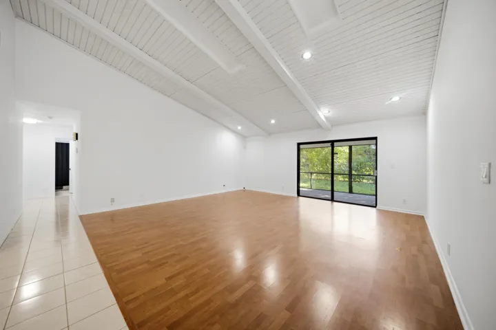 Spacious interior featuring a vaulted white plank ceiling with exposed beams, recessed lighting, and wood-finish flooring