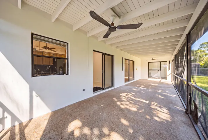 Spacious screened porch with a textured concrete floor, exposed beam ceiling, and multiple ceiling fans