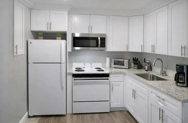 Well-appointed kitchen featuring white cabinetry, light-toned countertops, a stainless steel sink, wood-look vinyl flooring, and a stainless steel over-the-range microwave