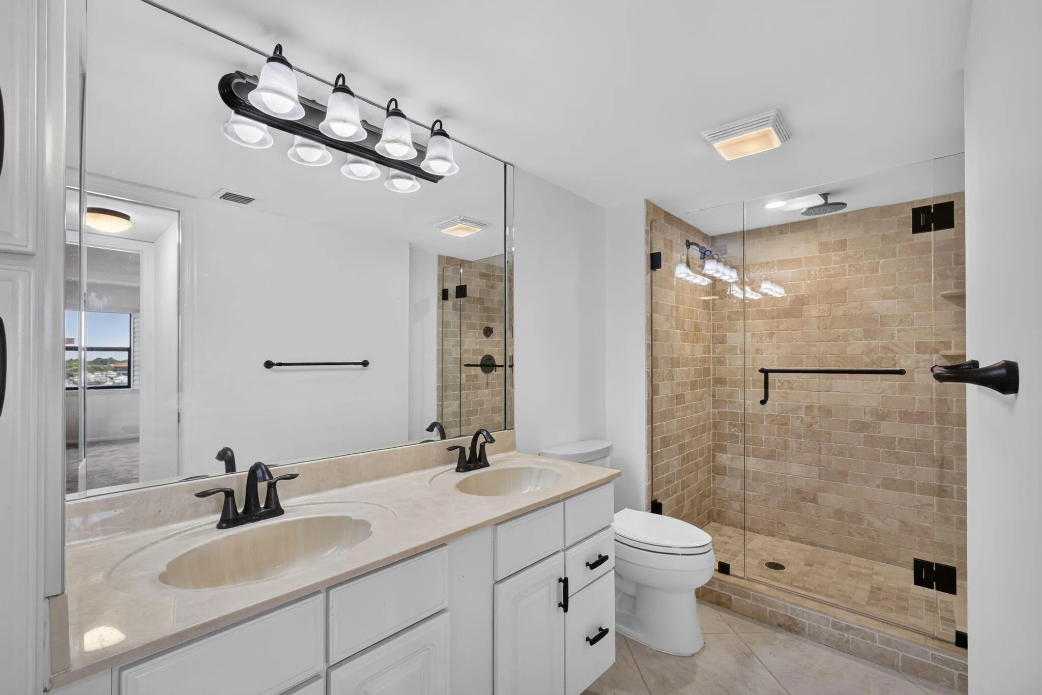 Bathroom featuring a double vanity with an integrated countertop, white cabinetry with dark hardware, and an expansive mirror