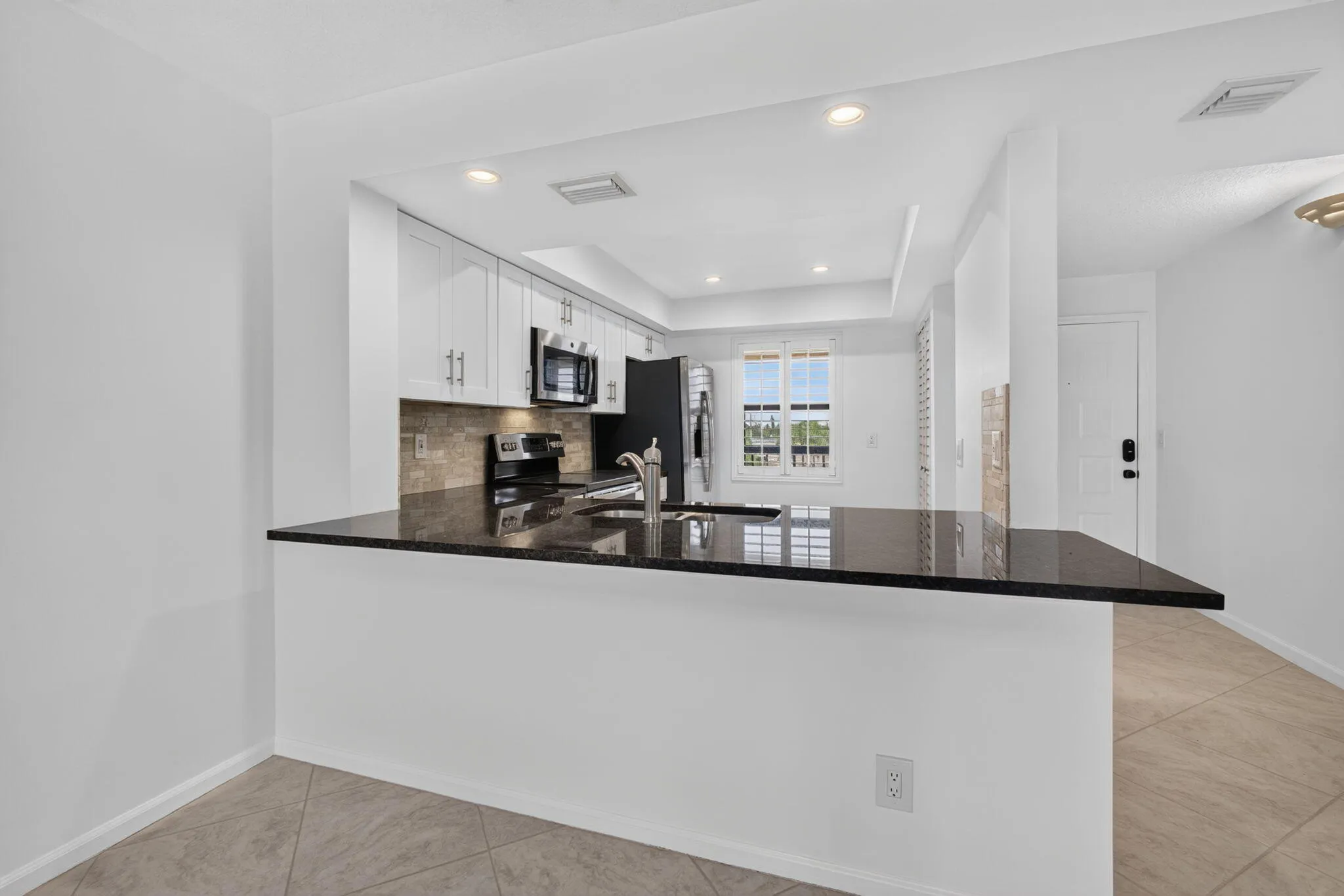 Open-concept kitchen featuring a peninsula with dark stone countertops, white cabinetry with silver hardware, a tile backsplash, and stainless steel appliances