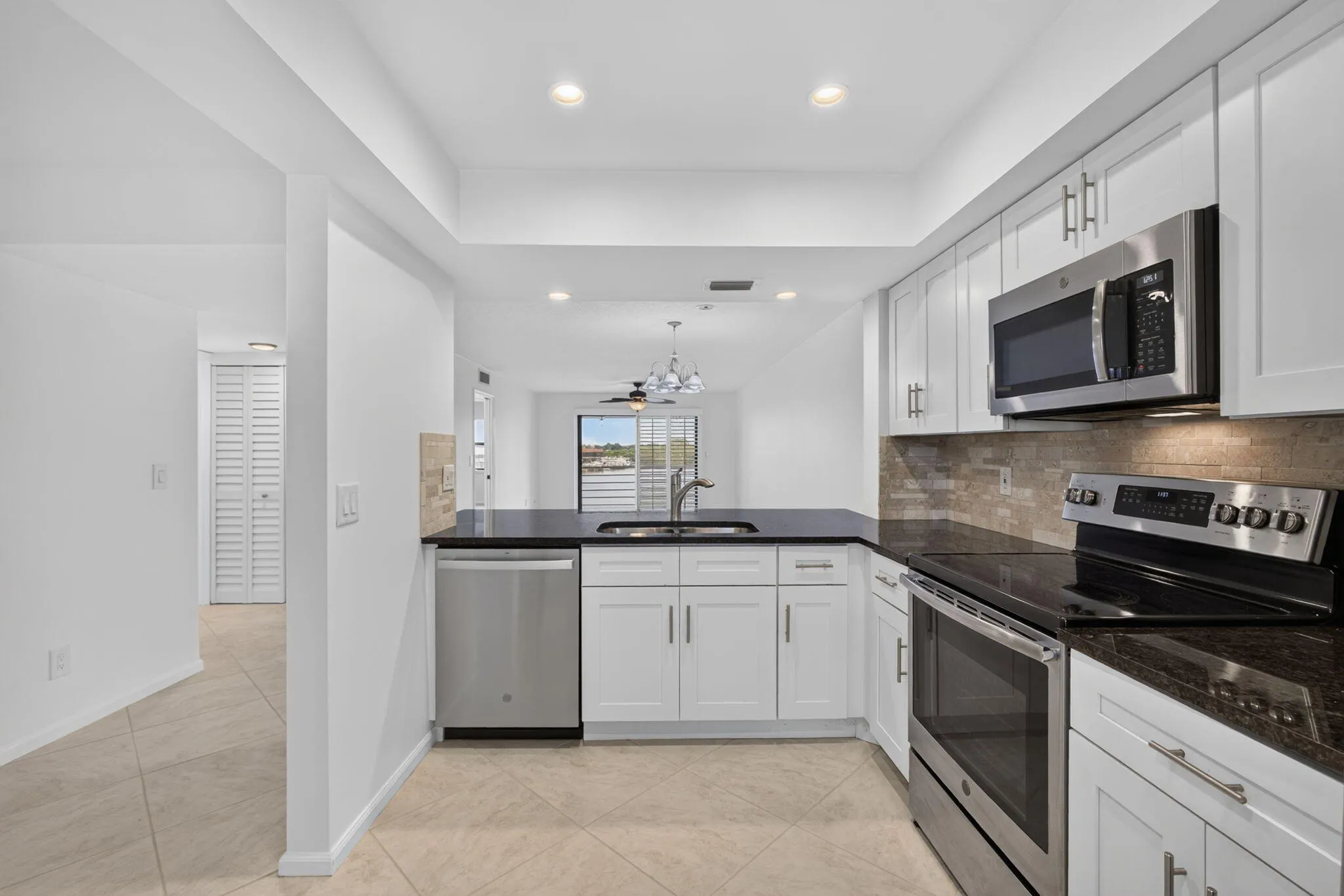 Kitchen featuring white shaker-style cabinetry, dark countertops, stainless steel appliances, and a tiled backsplash