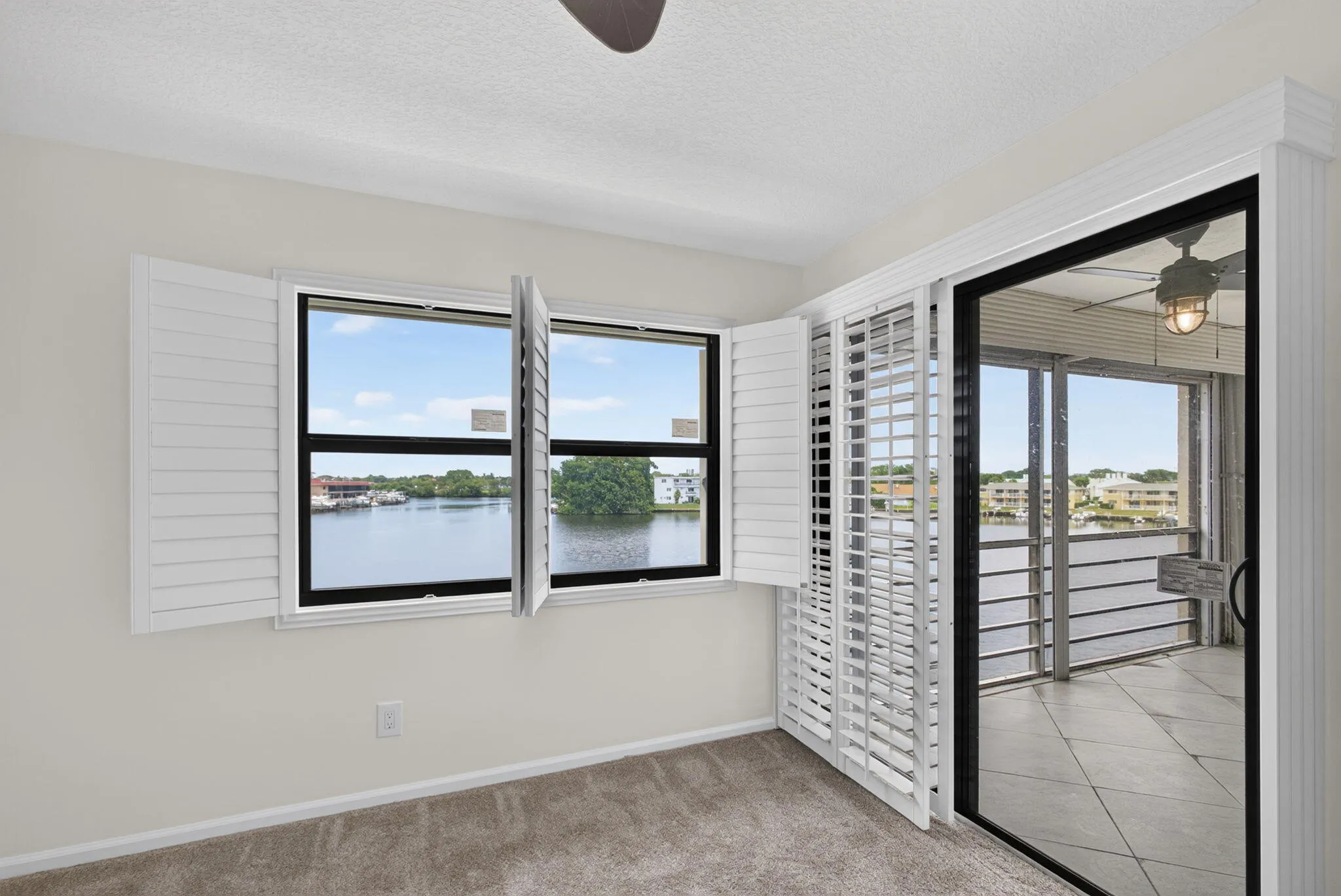 Waterfront views from expansive windows and sliding glass doors, featuring white plantation shutters and a screened balcony with tiled flooring