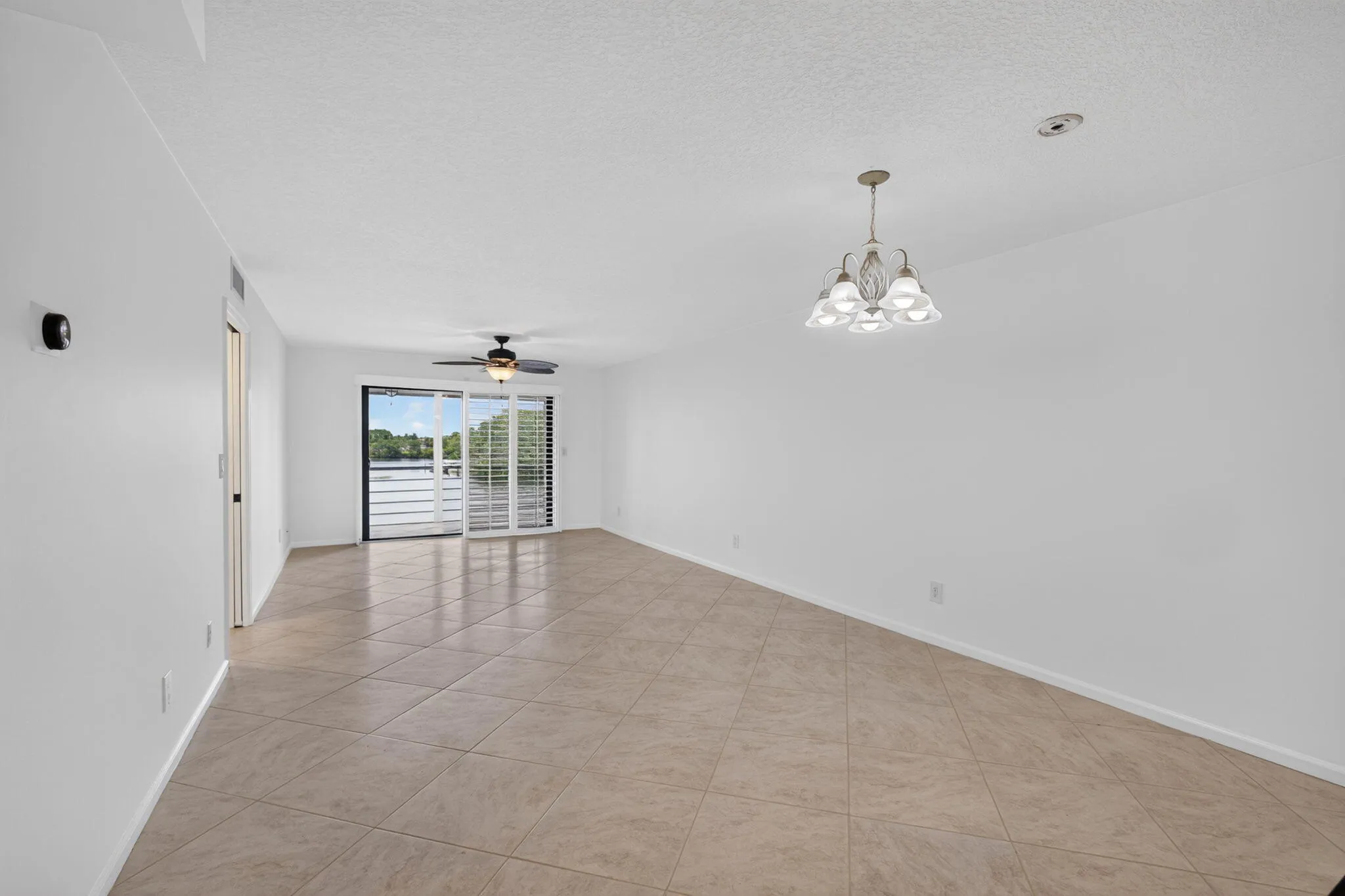 Expansive open living area featuring large format tile flooring, a ceiling fan, and a multi-light chandelier