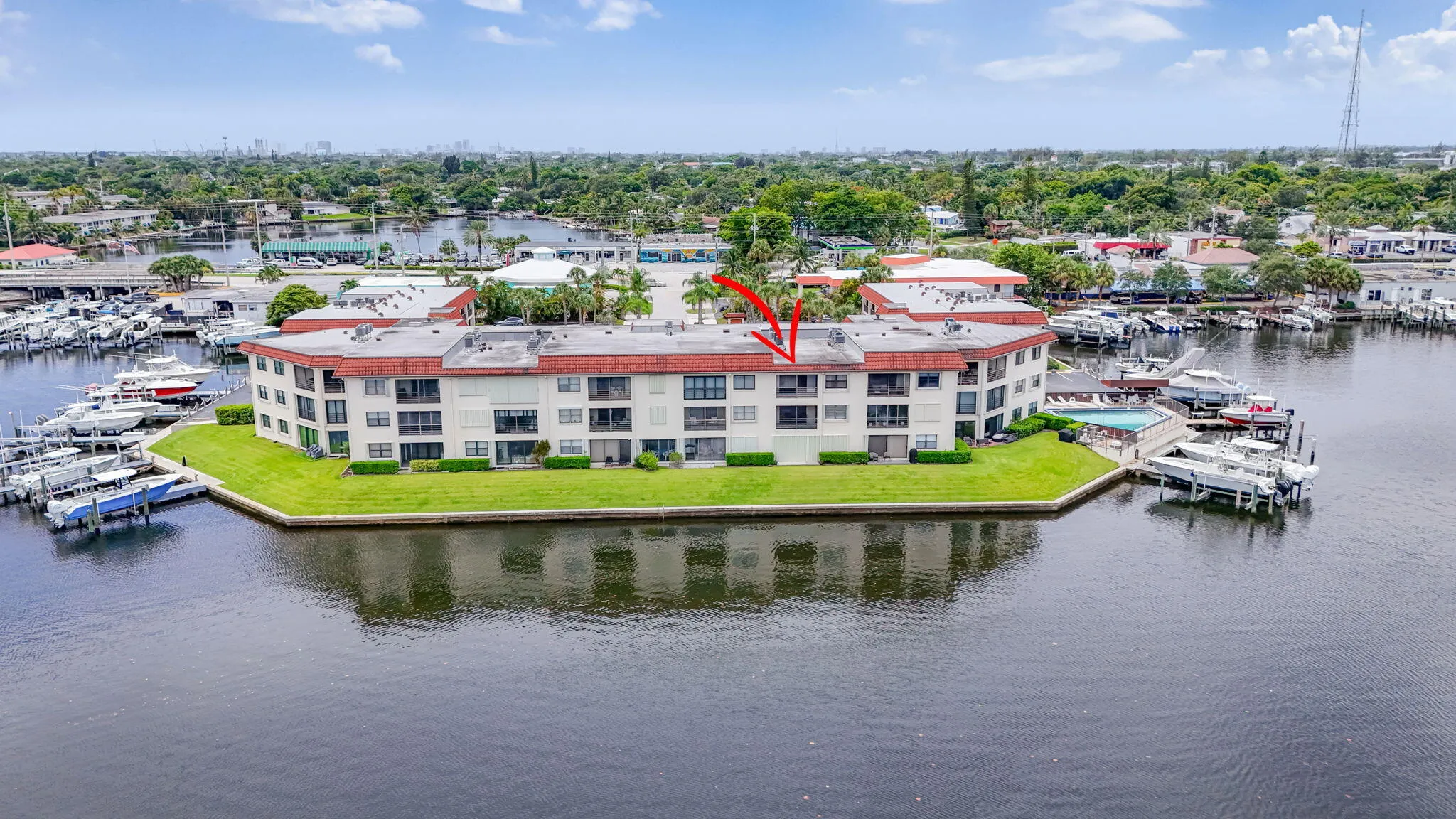 Waterfront multi-story building featuring a marina with multiple boat slips, a communal swimming pool, and dedicated green space