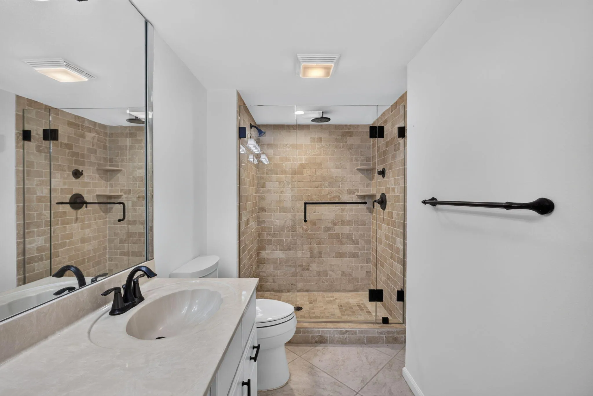 Bathroom featuring a glass-enclosed shower with brick-patterned tile, matte black fixtures, a built-in shower shelf, and a vanity with an integrated sink