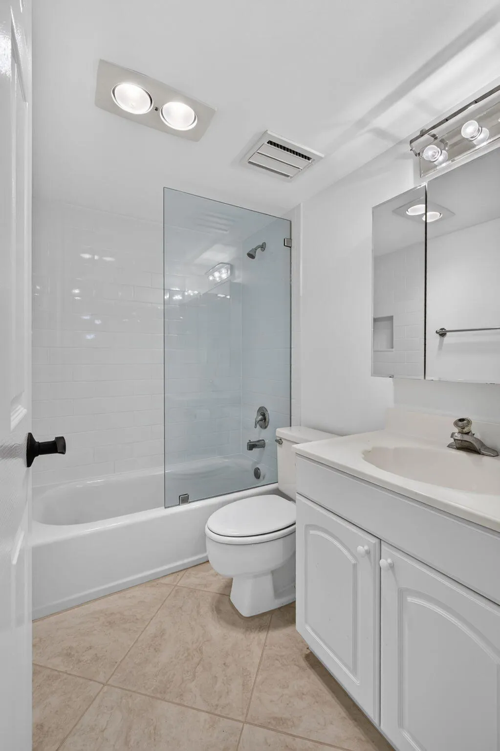 Bathroom featuring a glass shower enclosure over the tub, a single vanity with storage, a wall-mounted medicine cabinet, and tile flooring