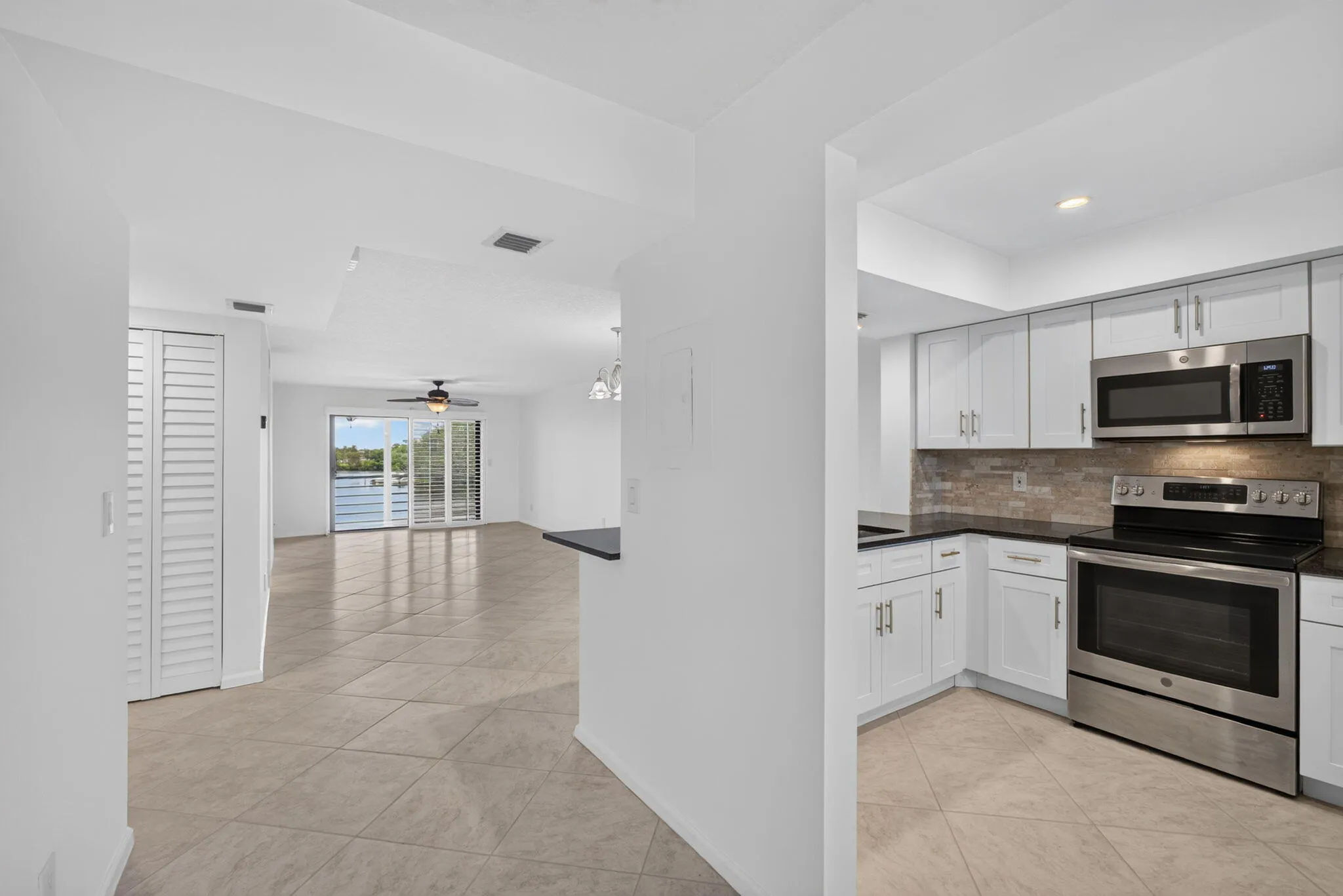 Modern kitchen featuring white cabinetry, stainless steel appliances, dark countertops, and a stone-finish backsplash