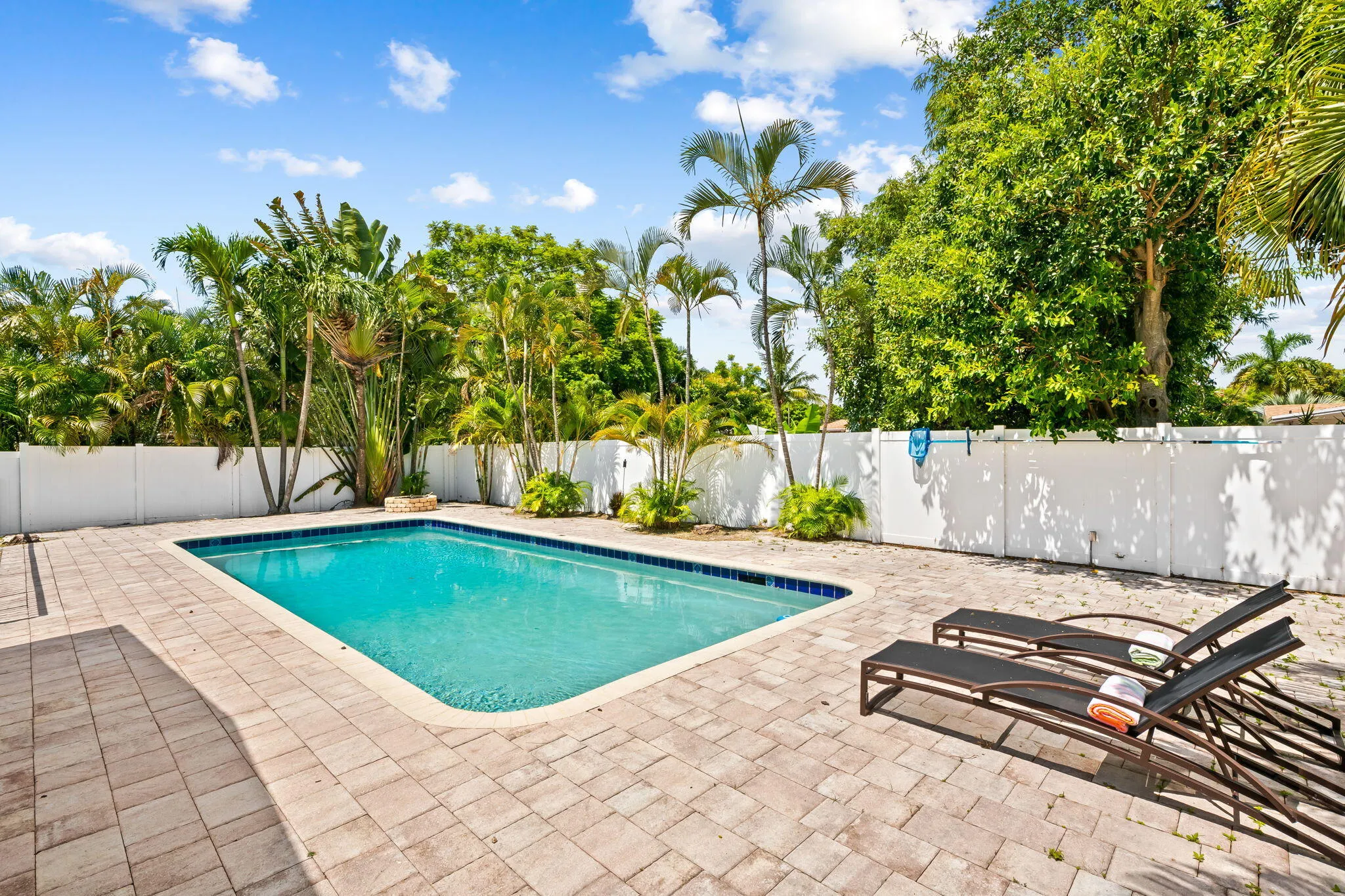 Outdoor swimming pool with a blue tile border, surrounded by a paver patio