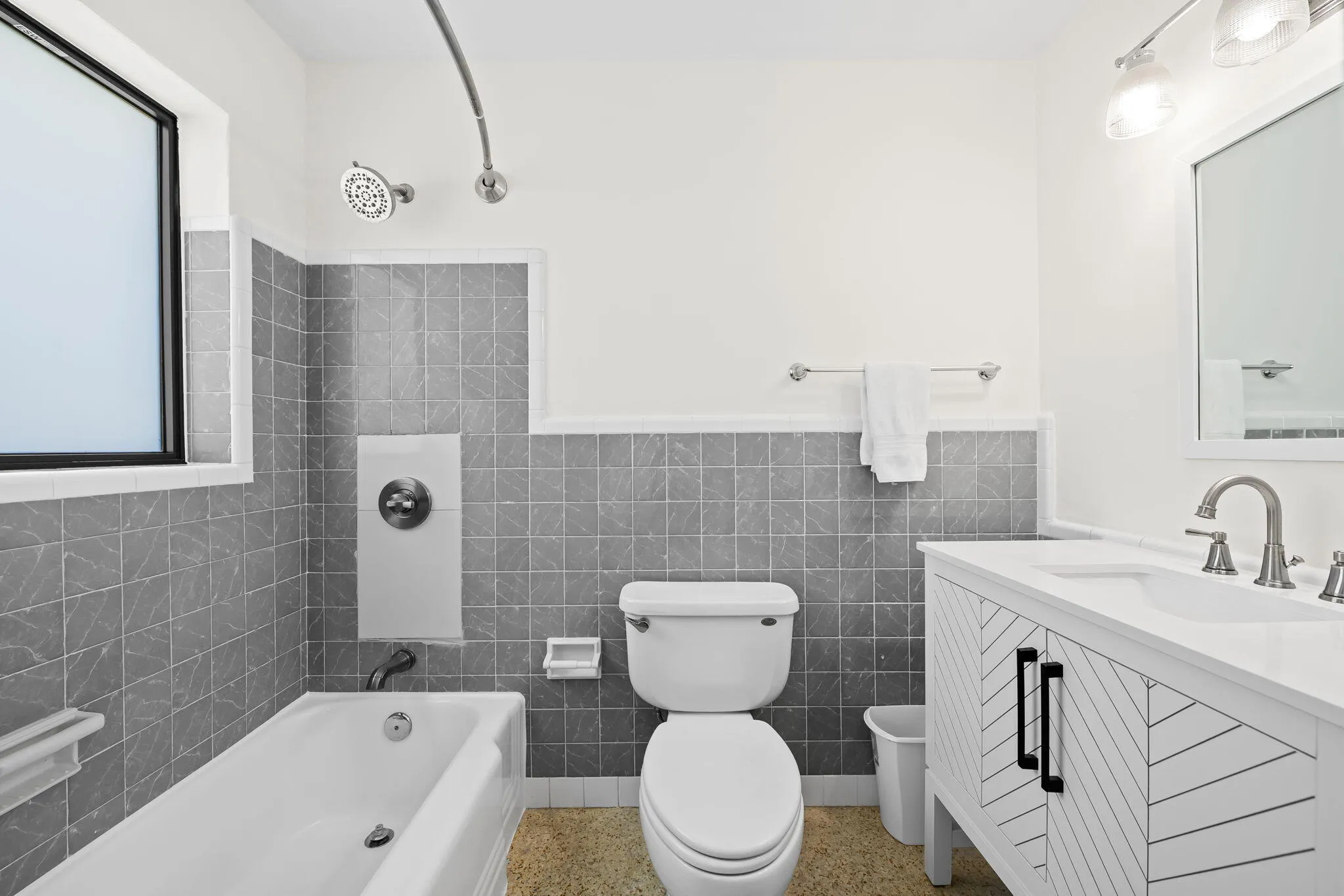 Bathroom featuring a white bathtub, grey wall tiling, and a modern vanity with a rectangular sink