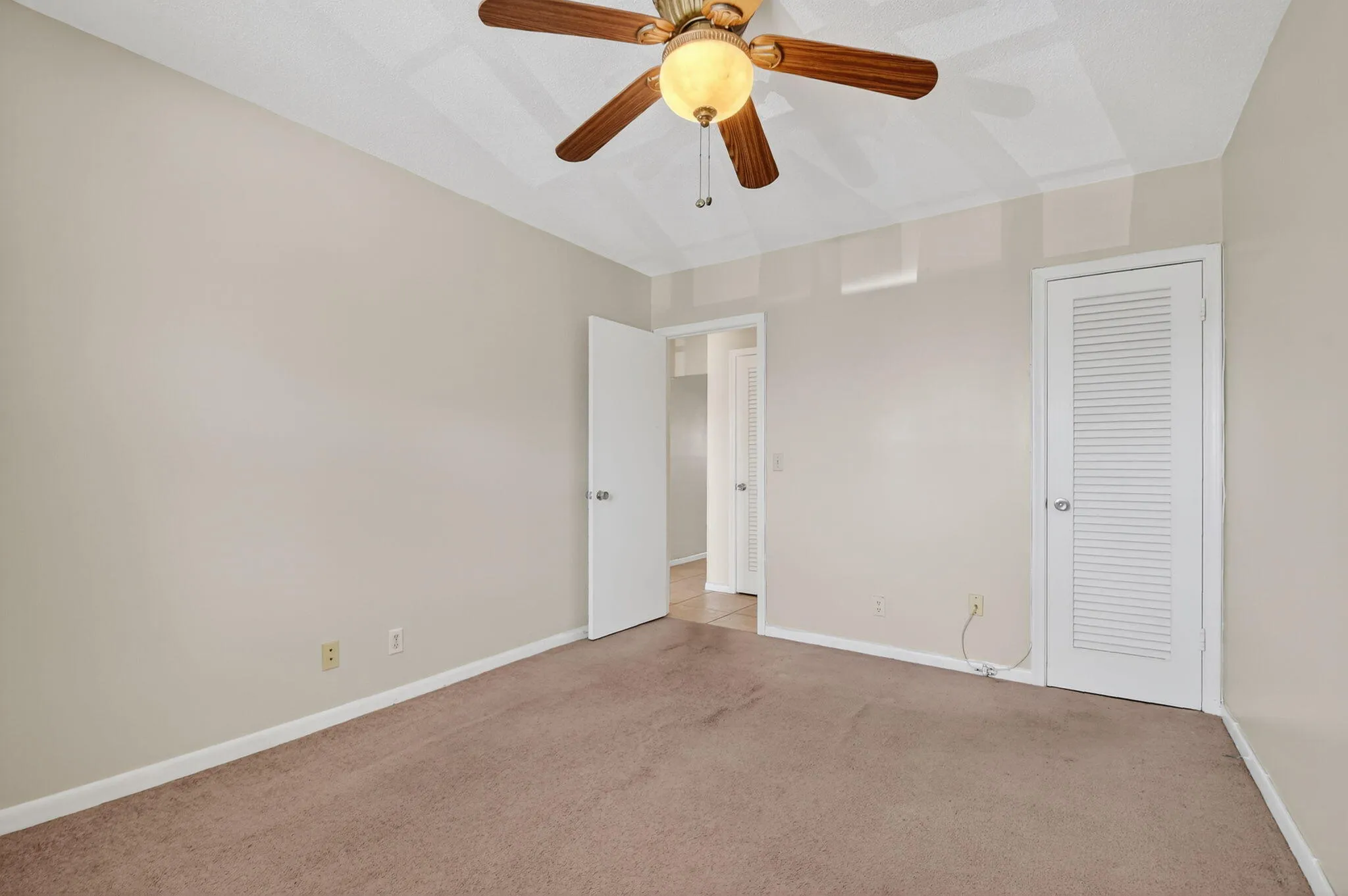 Carpeted room featuring a ceiling fan with light fixture, neutral wall paint, and white trim