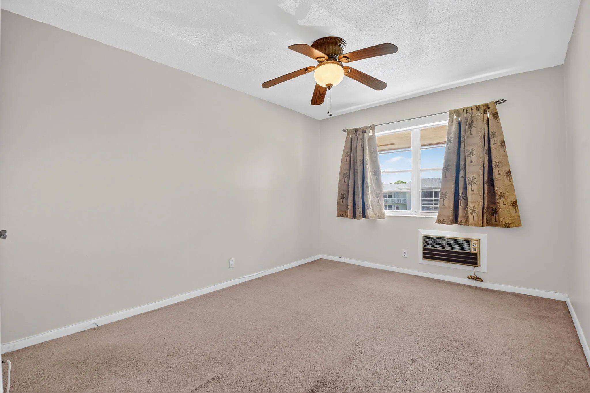 Carpeted room with a ceiling fan light fixture, a window with exterior views, and a wall-mounted air conditioning unit