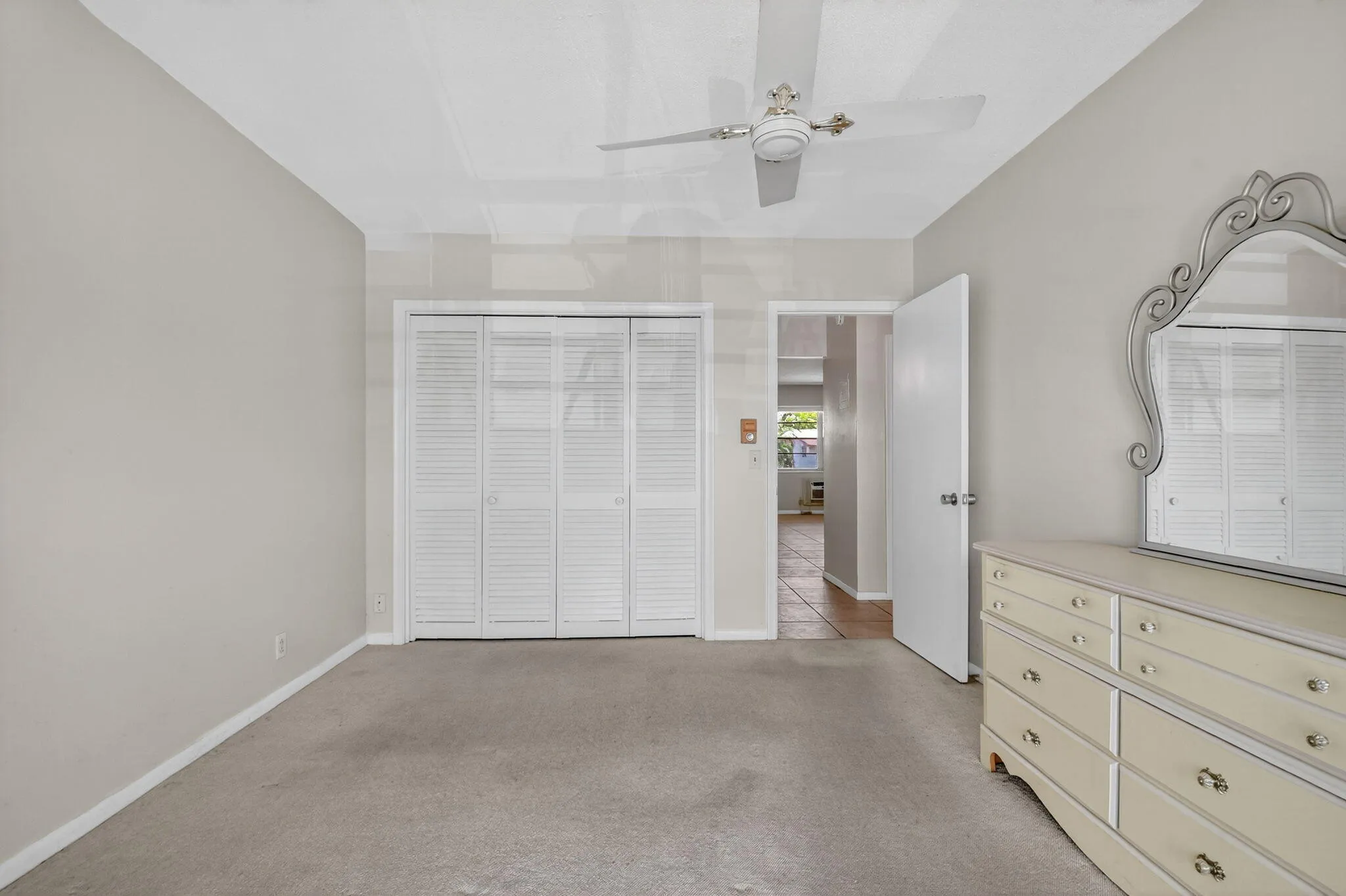 Carpeted interior space featuring neutral wall tones, bi-fold louvered closet doors, and a ceiling fan