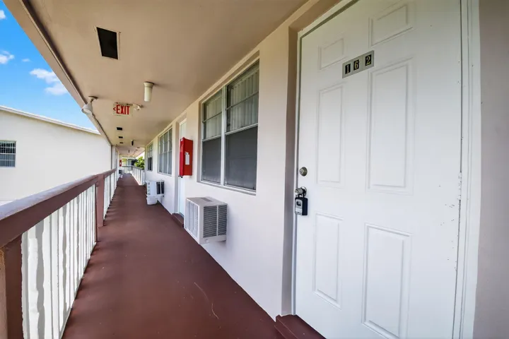 Exterior walkway featuring a white paneled entry door, a dark brown floor, and a white railing