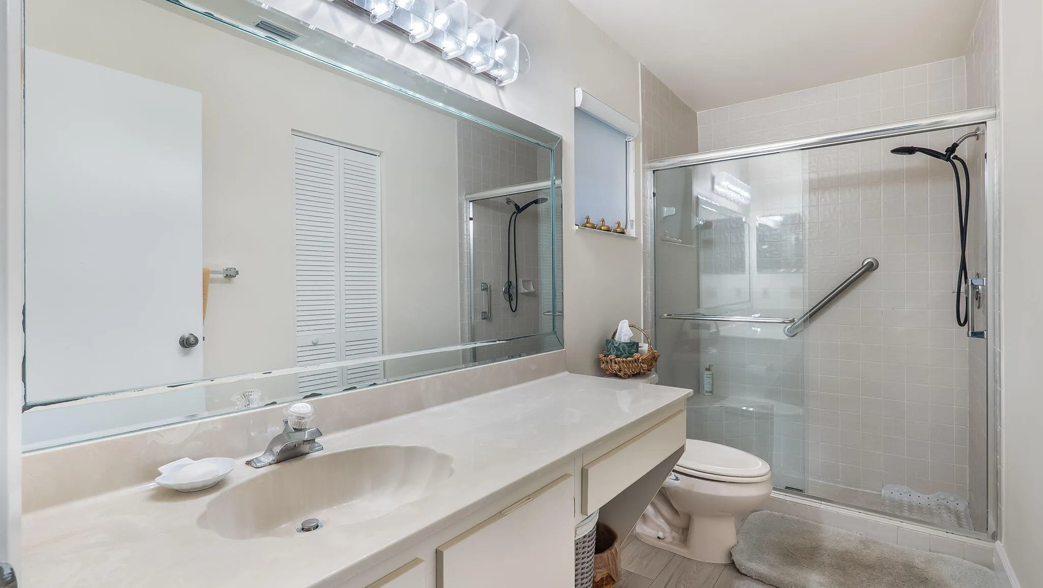 Bathroom featuring a vanity with an integrated sink, a large wall-mounted mirror, a modern light fixture, a tiled shower with a sliding glass door, and a built-in grab bar