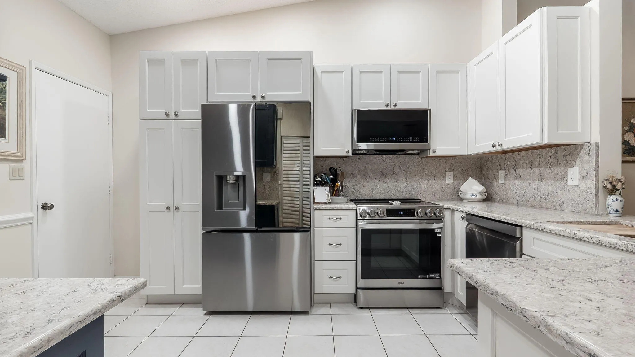 Kitchen featuring white shaker-style cabinetry, stainless steel appliances, and a light-toned granite countertop and backsplash