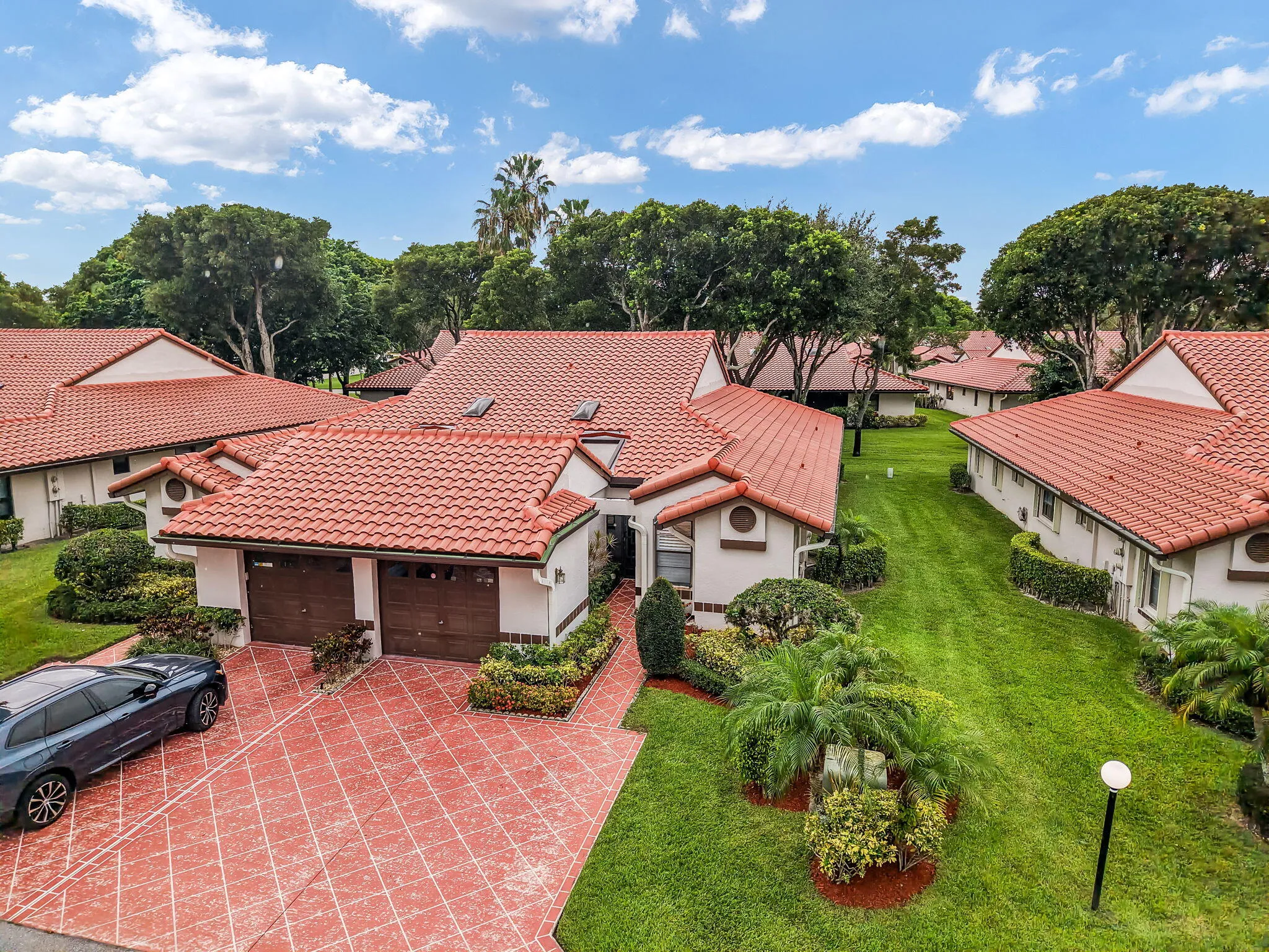 Spanish Colonial-inspired residence featuring a terracotta-tiled roof, a patterned paver driveway, and a two-car garage with wood-finish doors