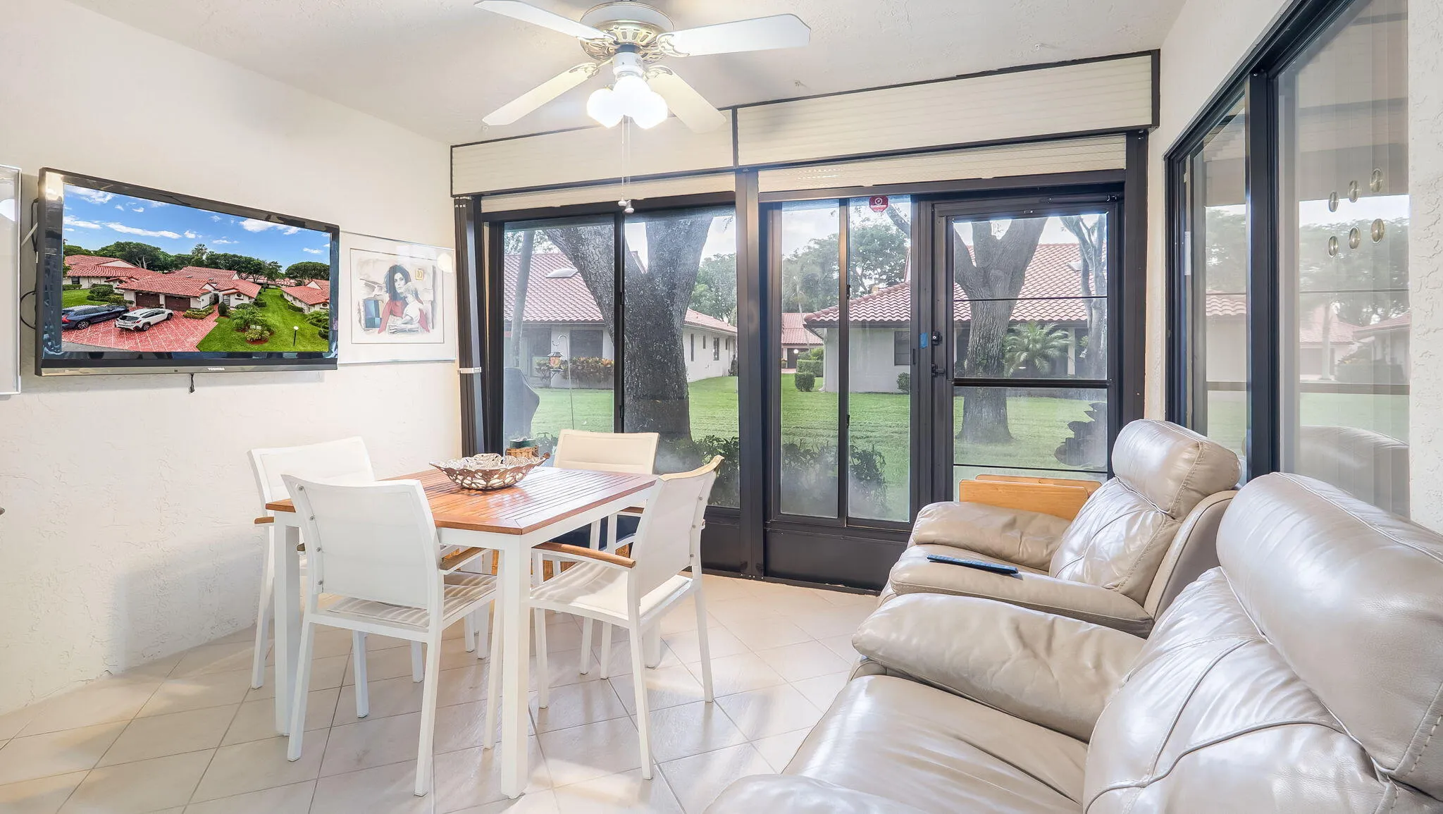 Enclosed sunroom featuring tile flooring, a ceiling fan with light fixture, and multiple sliding glass doors with roller shades