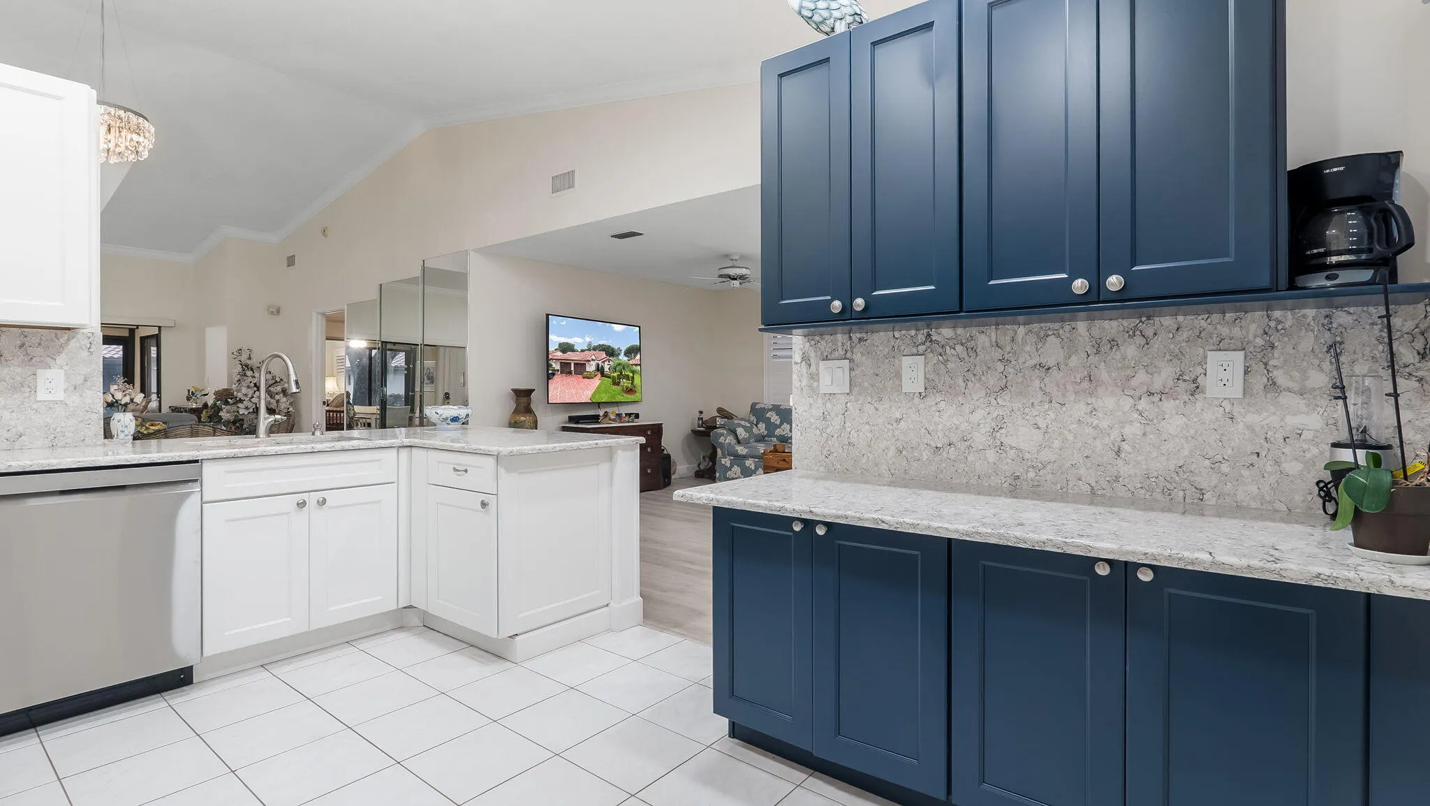 Kitchen featuring white tile flooring, stainless steel dishwasher, white lower cabinetry, blue upper and lower cabinetry, and light-toned stone countertops with matching backsplash
