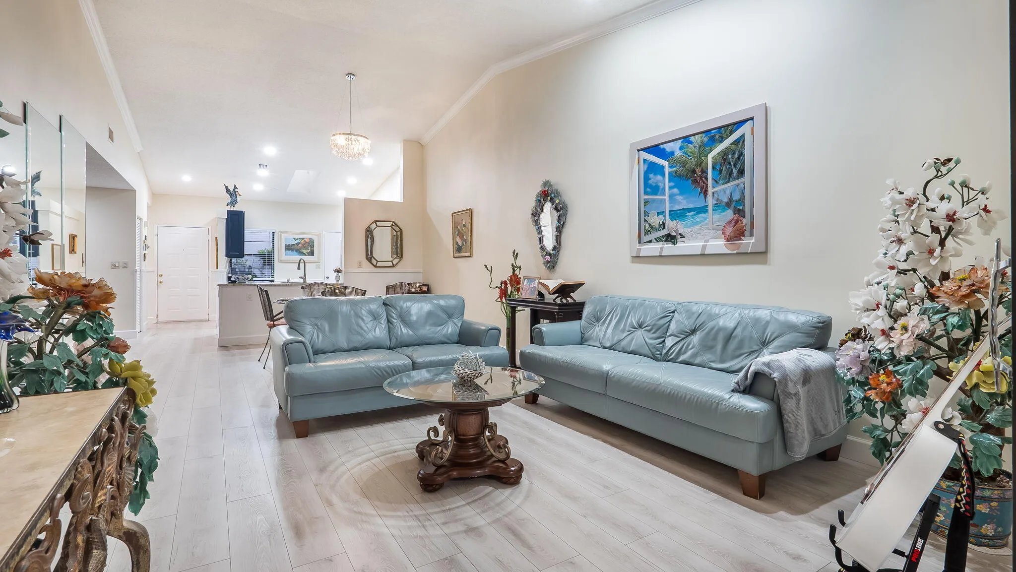 Spacious living area featuring light wood-finish flooring, vaulted ceilings, recessed lighting, a decorative chandelier, and a partial view of the kitchen island