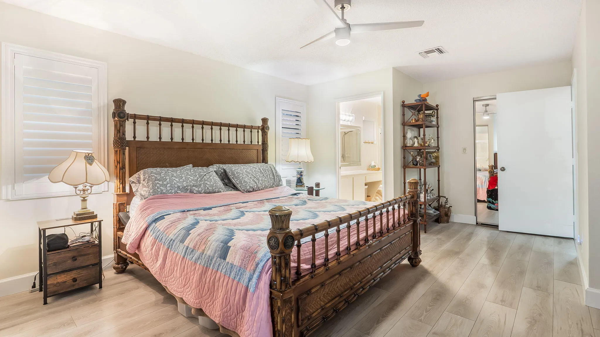 Spacious bedroom featuring wood-finish flooring, white plantation shutters, and a ceiling fan