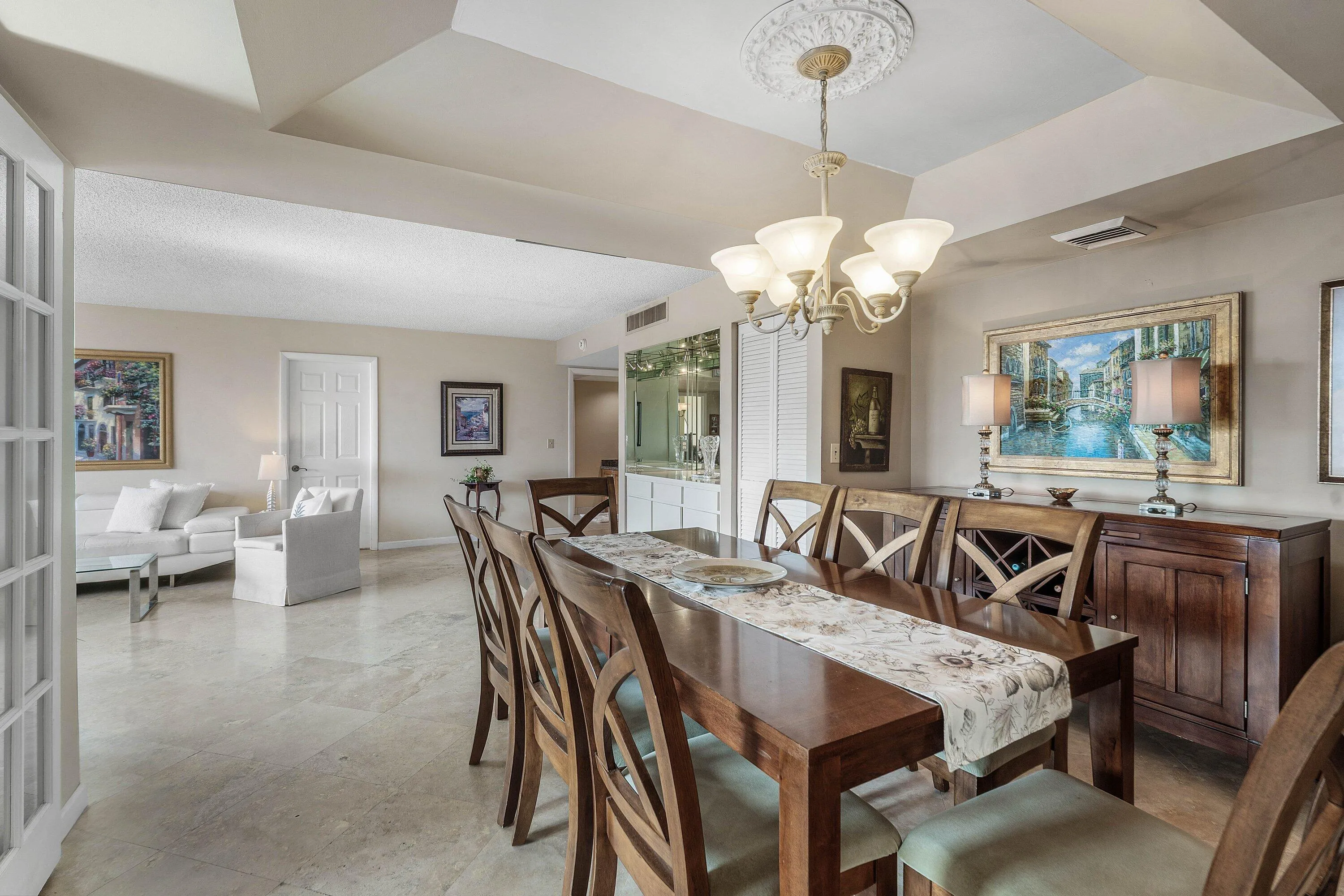 Dining area featuring a tray ceiling with an ornate medallion and chandelier, marble-finish flooring, and a built-in wet bar with mirrored accents