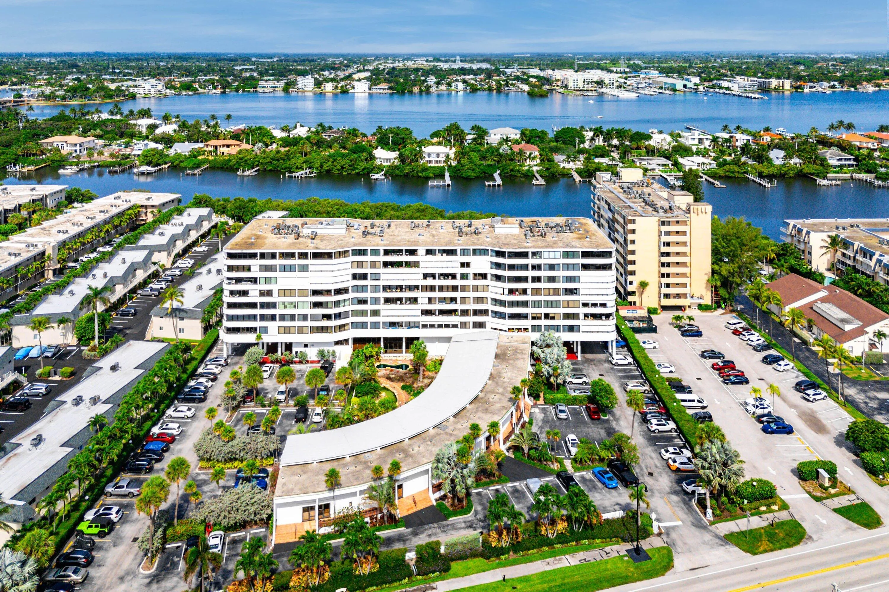 Multi-story building featuring numerous balconies, a lushly landscaped entrance, and expansive parking areas