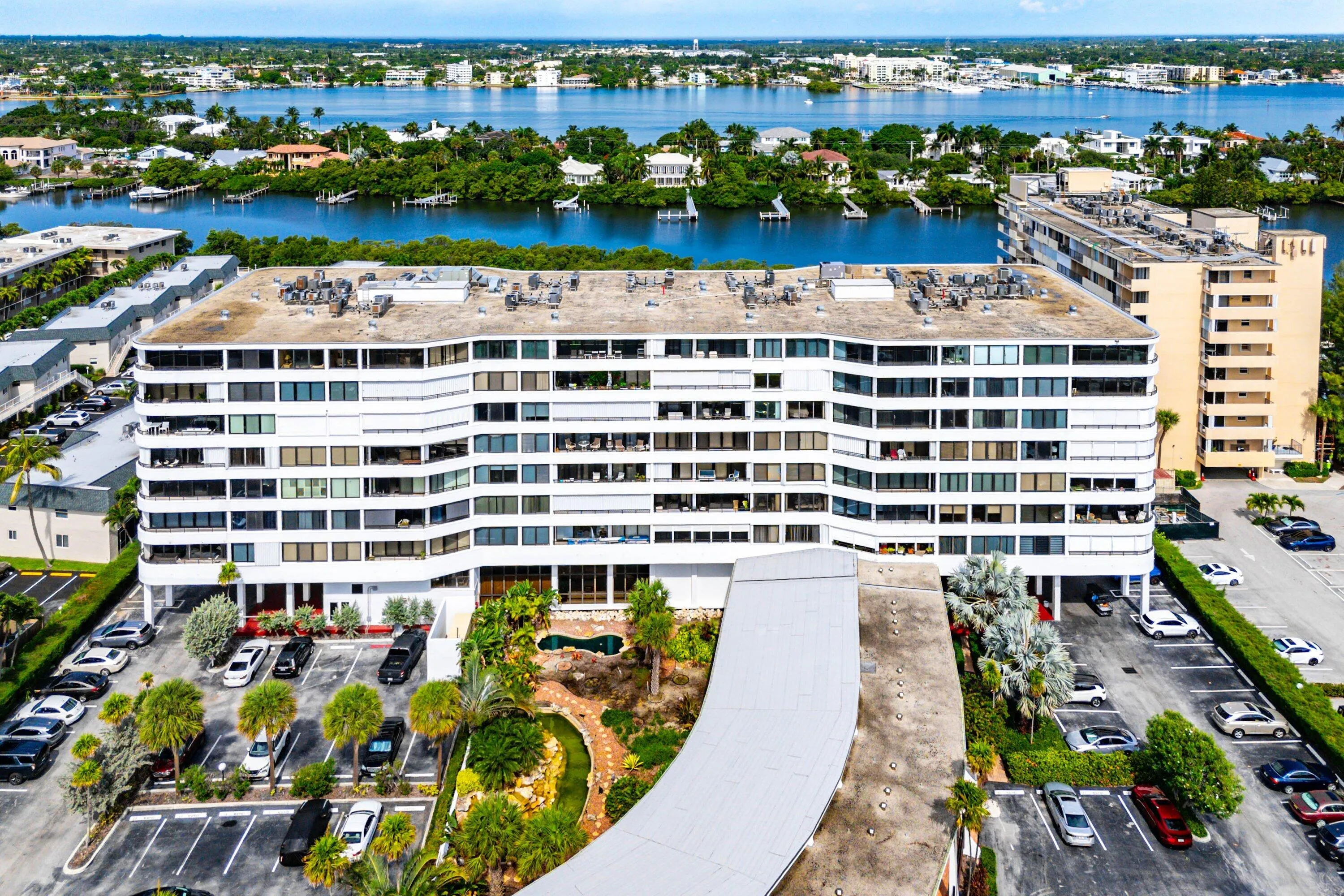 Multi-story white facade structure featuring private balconies, ample parking, and a lush landscaped courtyard with a pool