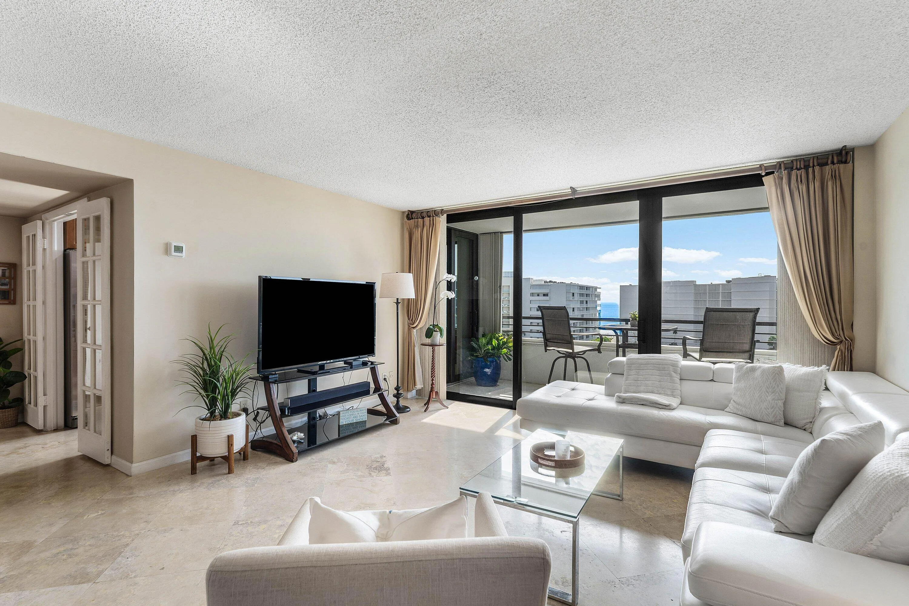 Living area with large format tile flooring and extensive impact glass doors opening to balcony