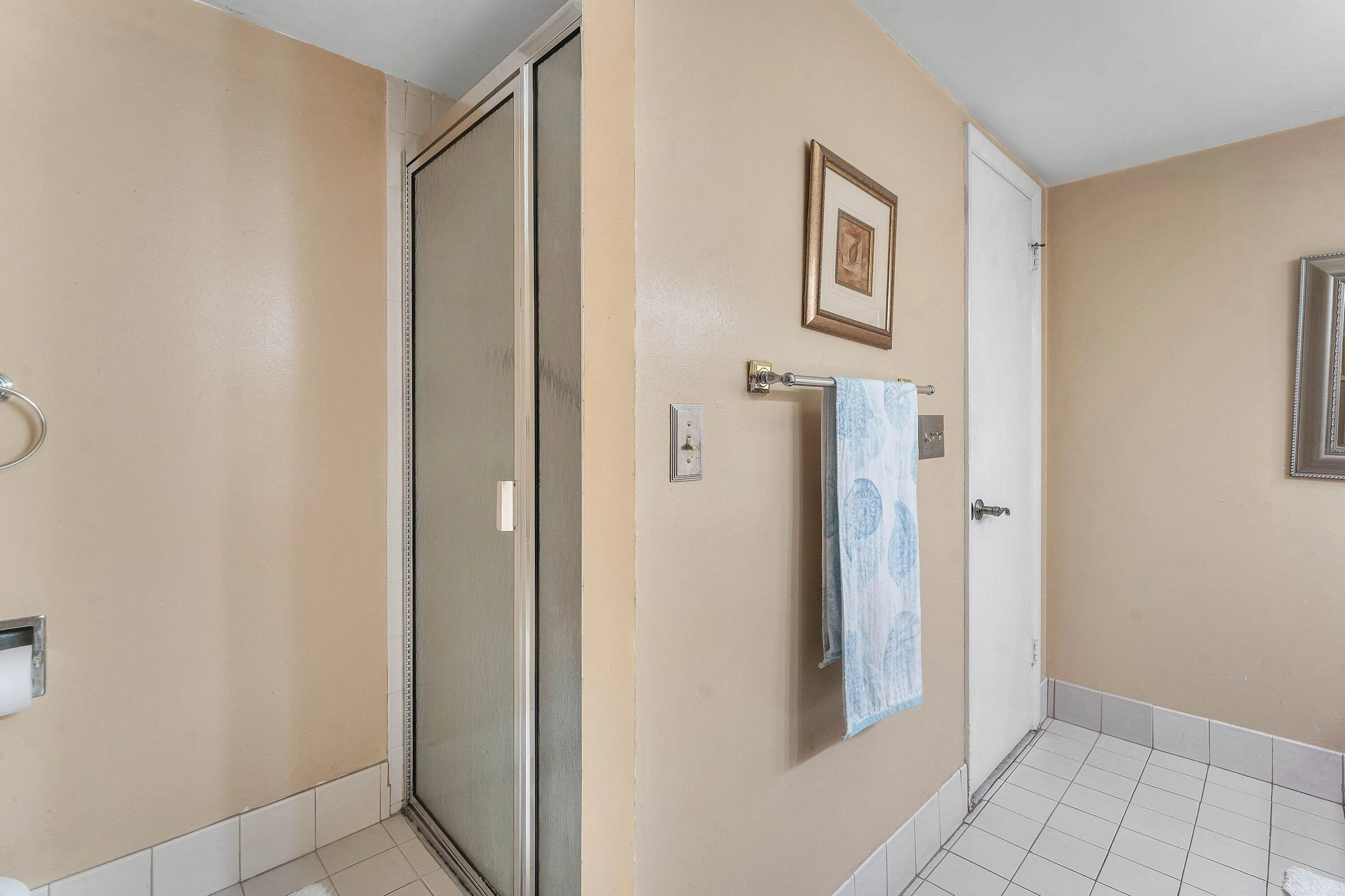 Walk-in shower with frosted glass enclosure and chrome hardware, complemented by white square floor tiling and baseboard trim