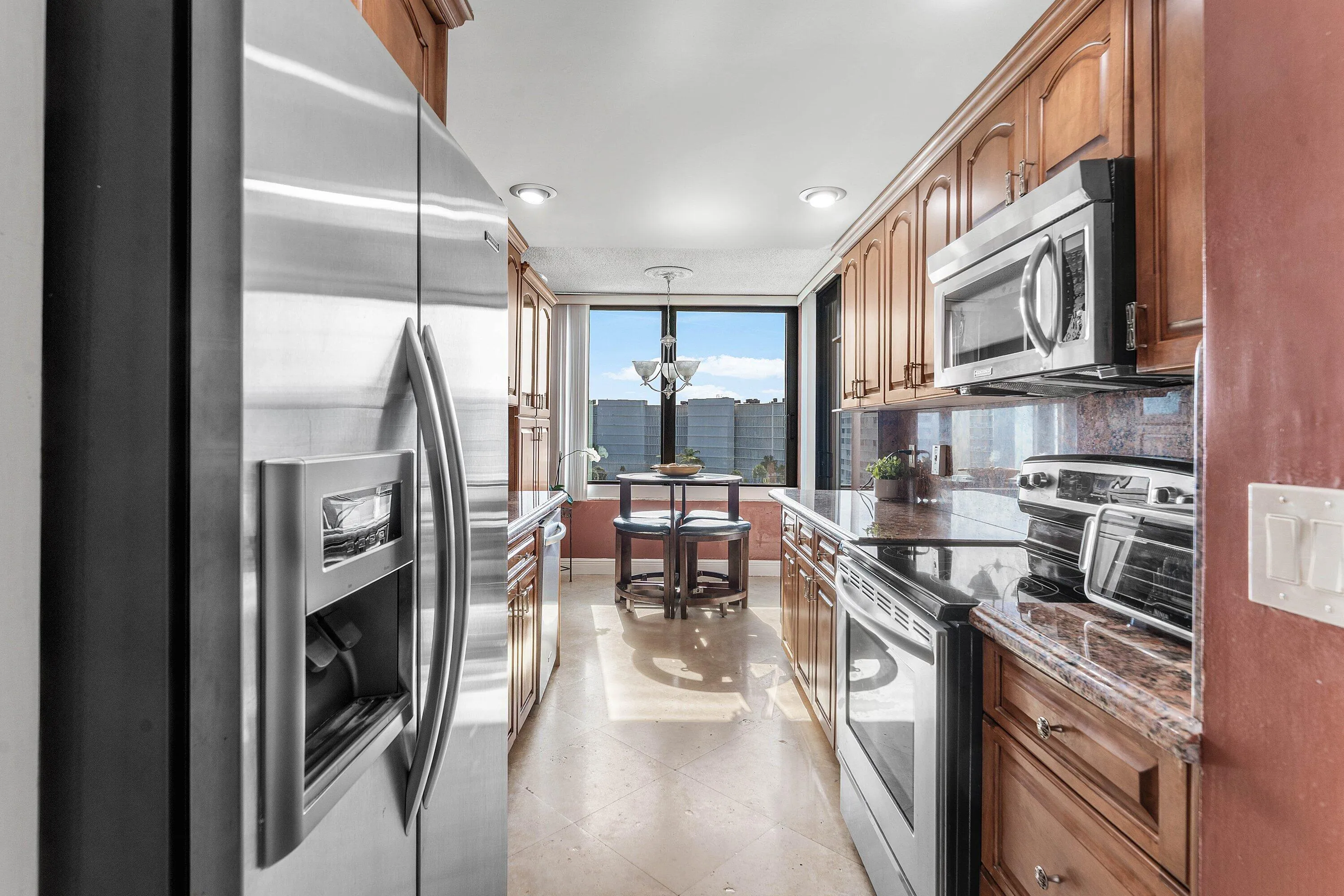 Galley kitchen featuring wood cabinetry, stainless steel appliances, dark stone countertops, and recessed lighting