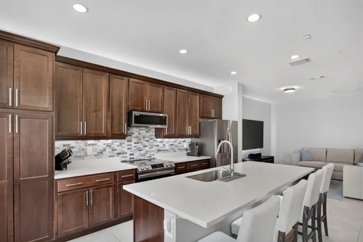 Spacious kitchen featuring dark wood cabinetry, white countertops, stainless steel appliances, a mosaic tile backsplash, and recessed lighting