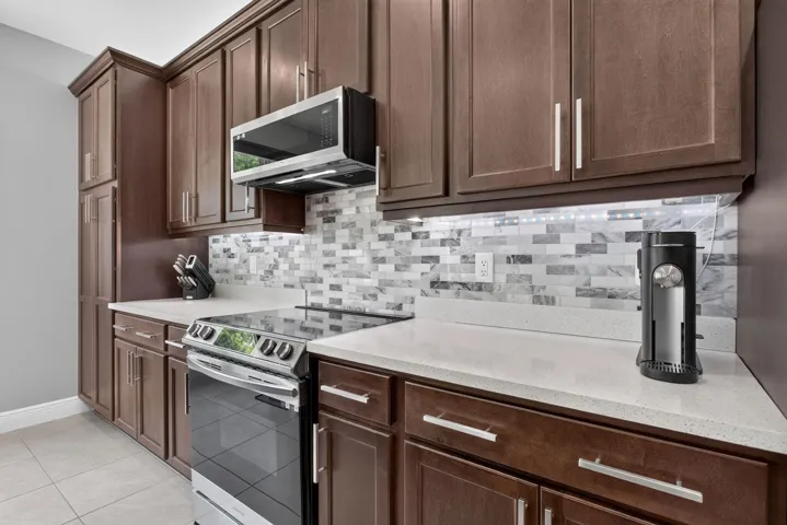 Modern kitchen featuring a breakfast bar island with seating, stainless steel appliances, dark wood cabinetry, a tile backsplash, and recessed lighting