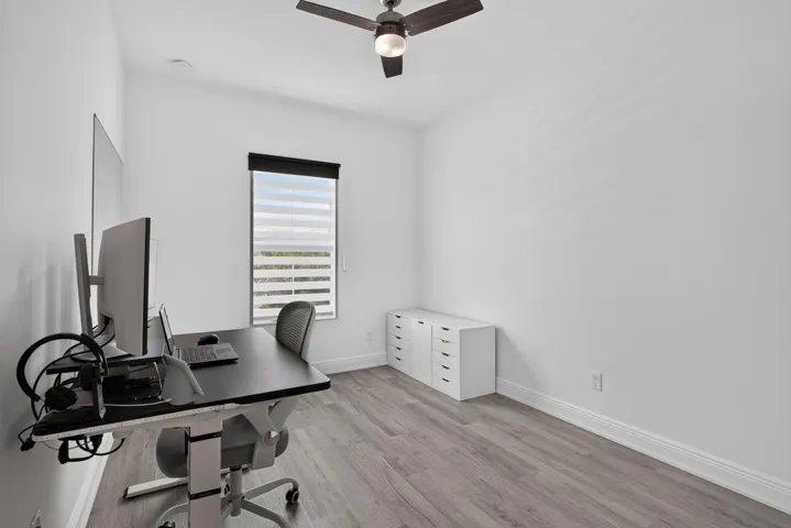 Room featuring wood-finish flooring, a window with horizontal blinds, a ceiling fan with integrated lighting, and white baseboards