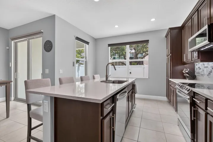 Kitchen featuring a large central island with light-toned countertops, dark wood-finish cabinetry, stainless steel appliances, and tile flooring