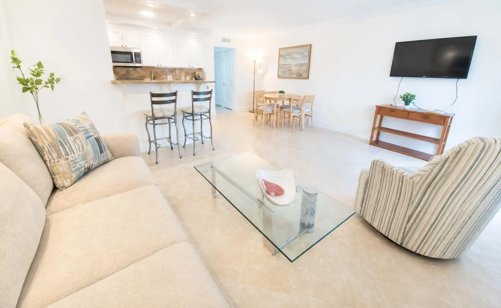 Open-concept living space with tile flooring throughout, featuring a kitchen peninsula with a breakfast bar, white cabinetry, and stainless steel appliances