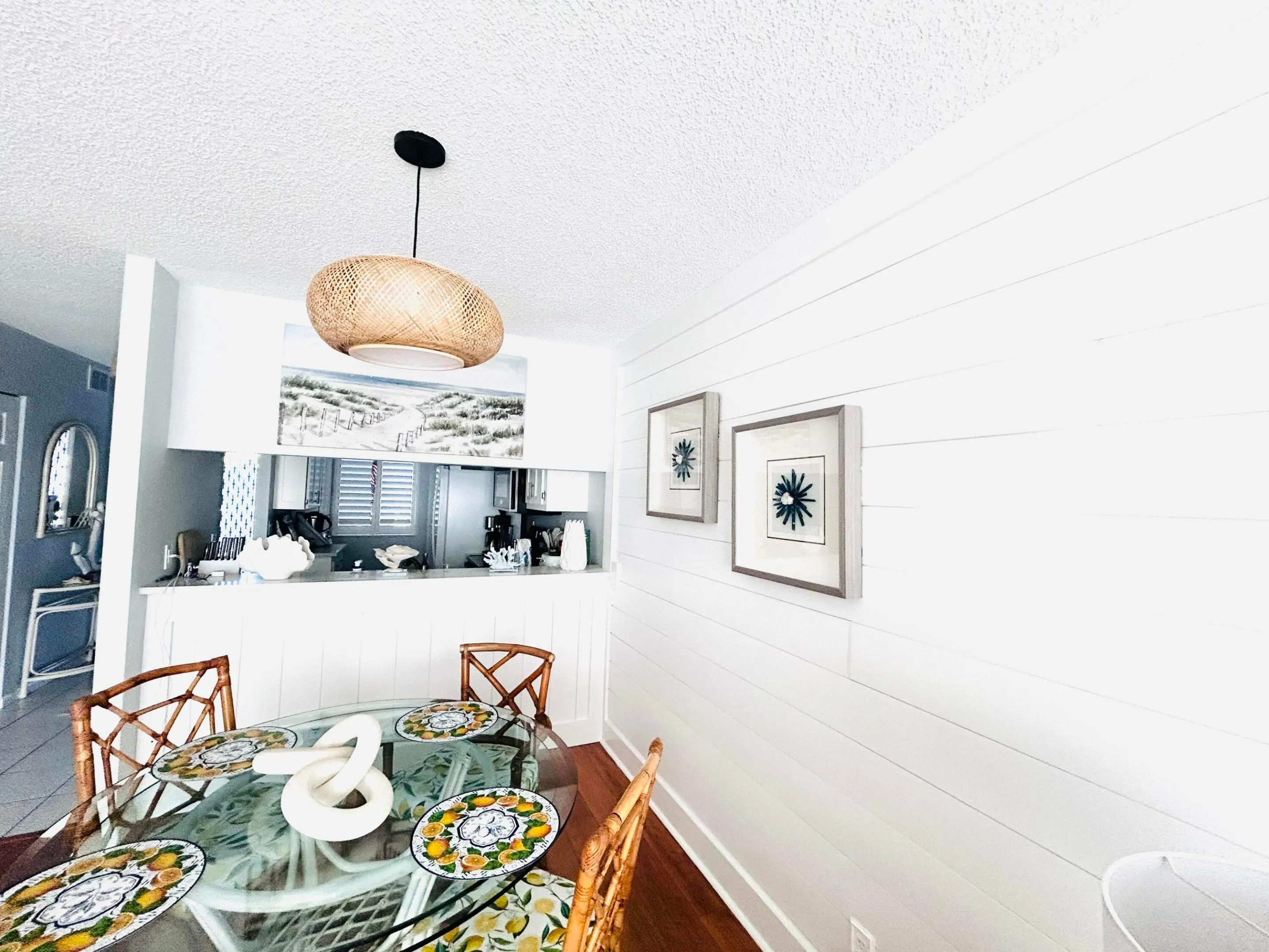 Dining area featuring a glass-top table, a woven pendant light fixture, and white shiplap wall paneling