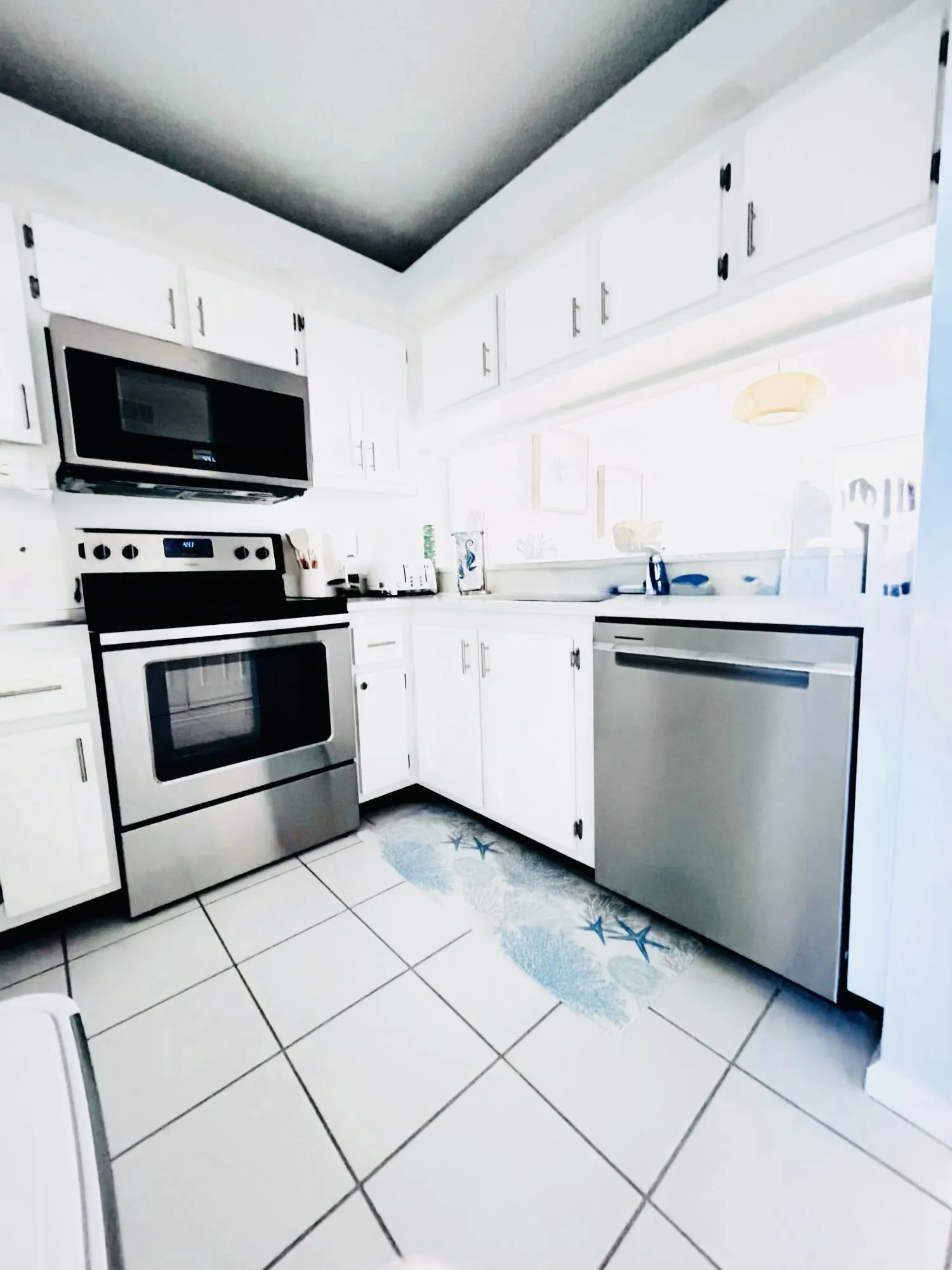 Kitchen featuring white cabinetry with dark hardware, a stainless steel range with an over-the-range microwave, a stainless steel dishwasher, and white square tile flooring