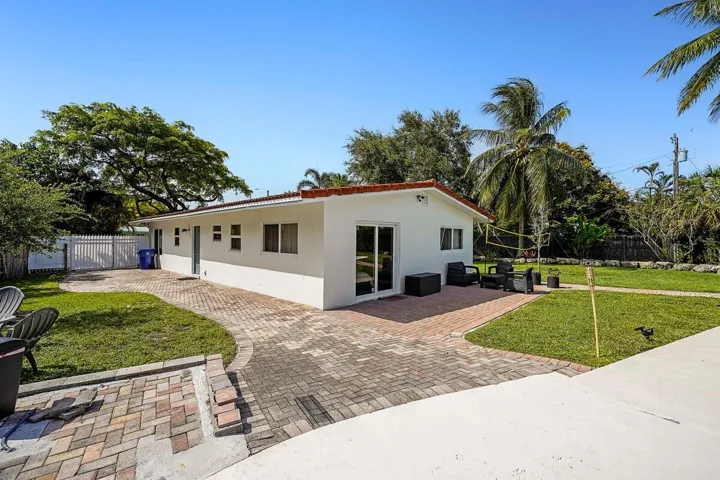 White stucco exterior with a terra cotta tile roof, brick paver patio, sliding glass door, and a manicured lawn