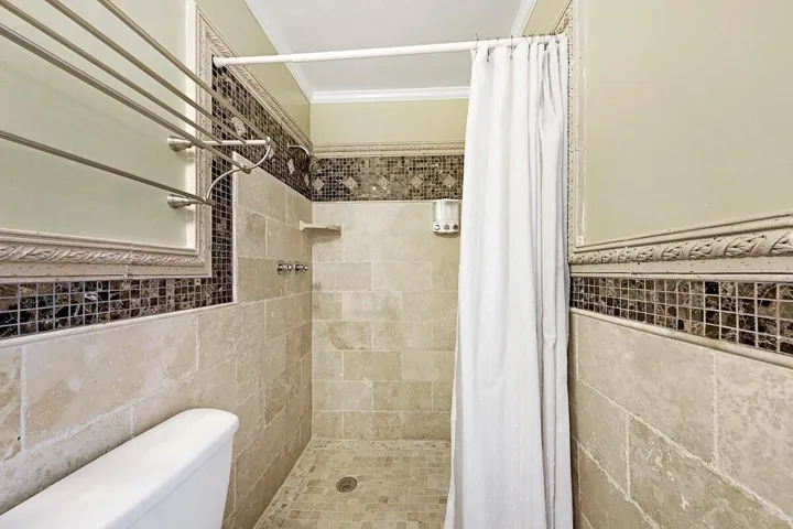 Tiled shower with a mosaic accent band, integrated shelf, and an adjacent toilet