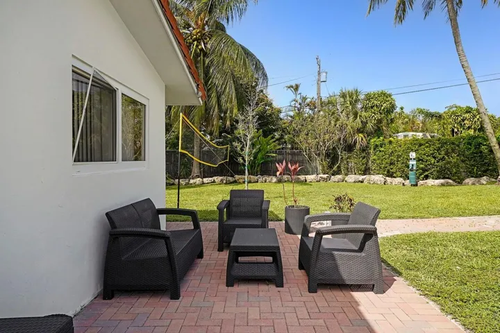 Brick paver patio extending to a manicured lawn, bordered by tropical foliage and mature palm trees