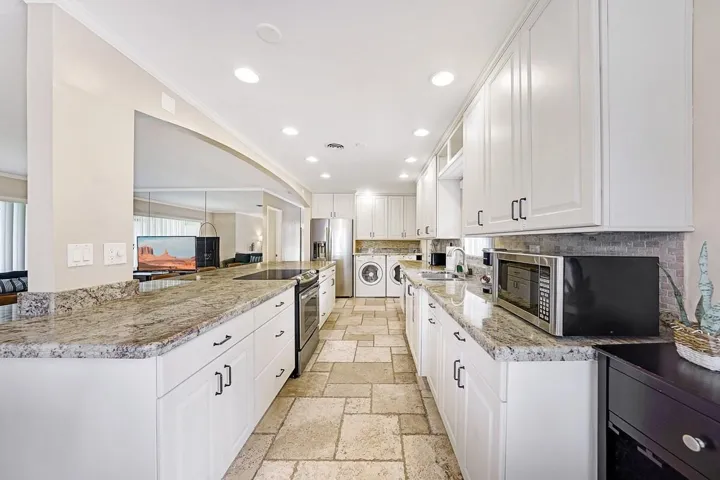 Galley kitchen featuring stone tile flooring, white cabinetry, integrated stainless steel appliances, granite countertops, and recessed lighting