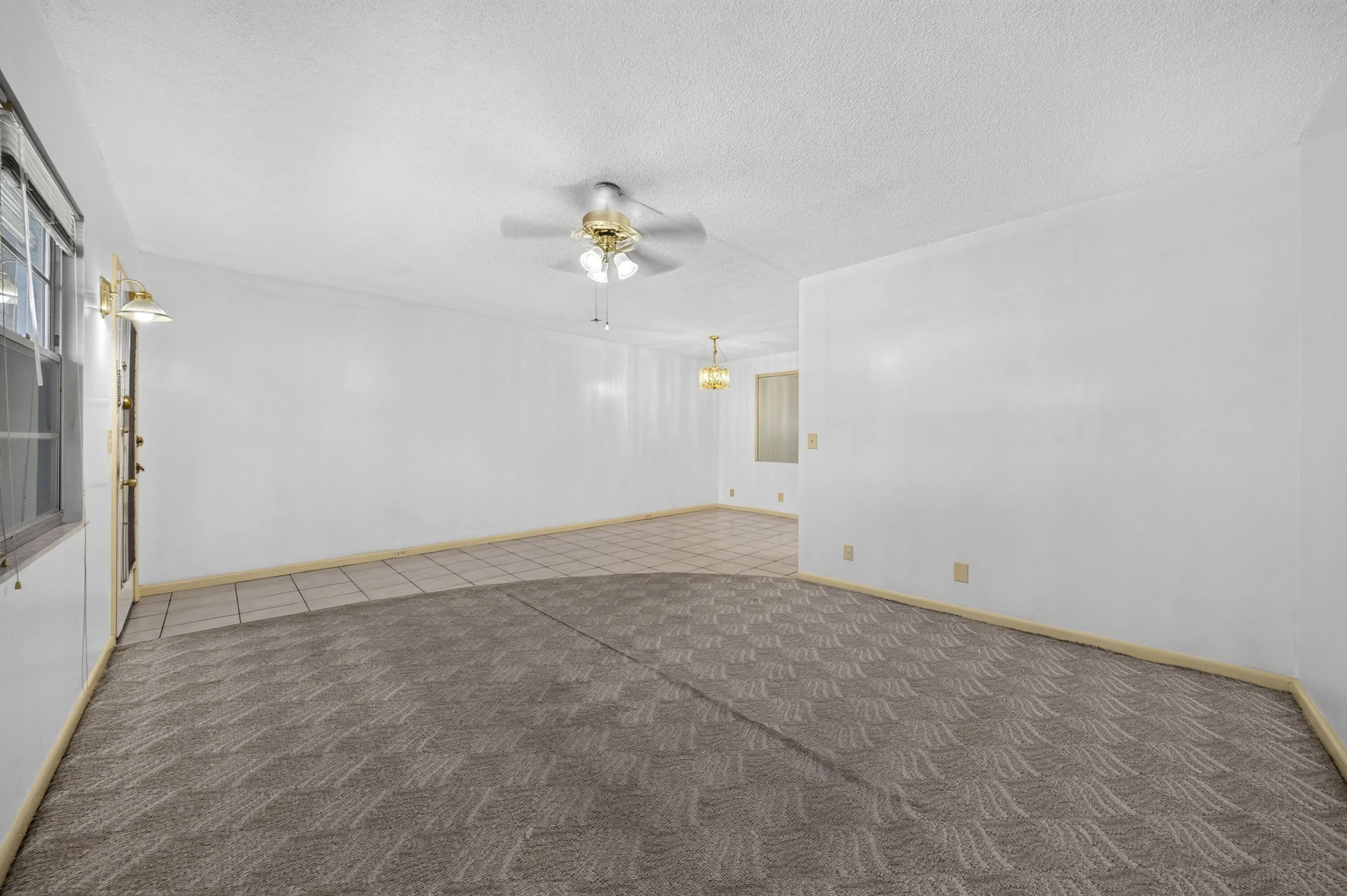 Spacious room featuring a combination of patterned carpet and tile flooring, a ceiling fan with integrated lighting, and multiple windows