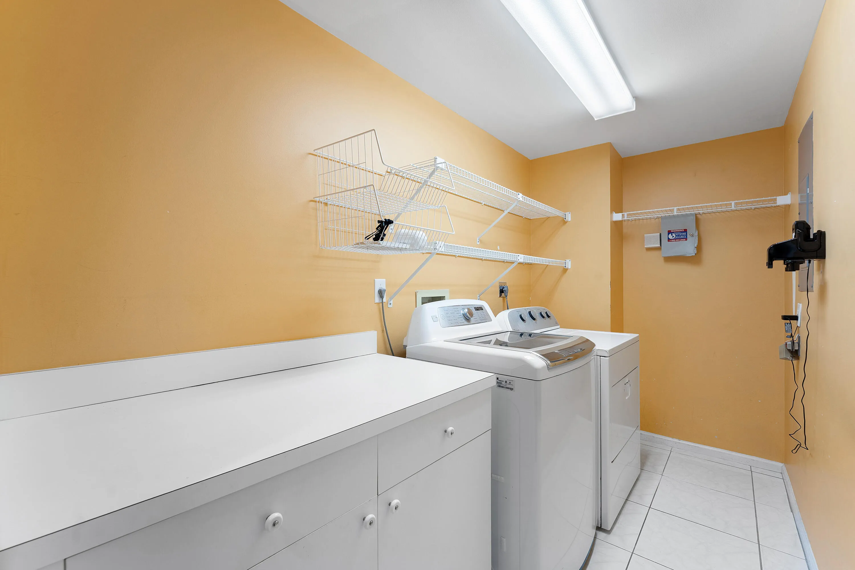Dedicated utility room featuring a built-in countertop, white base cabinetry, and overhead wire shelving