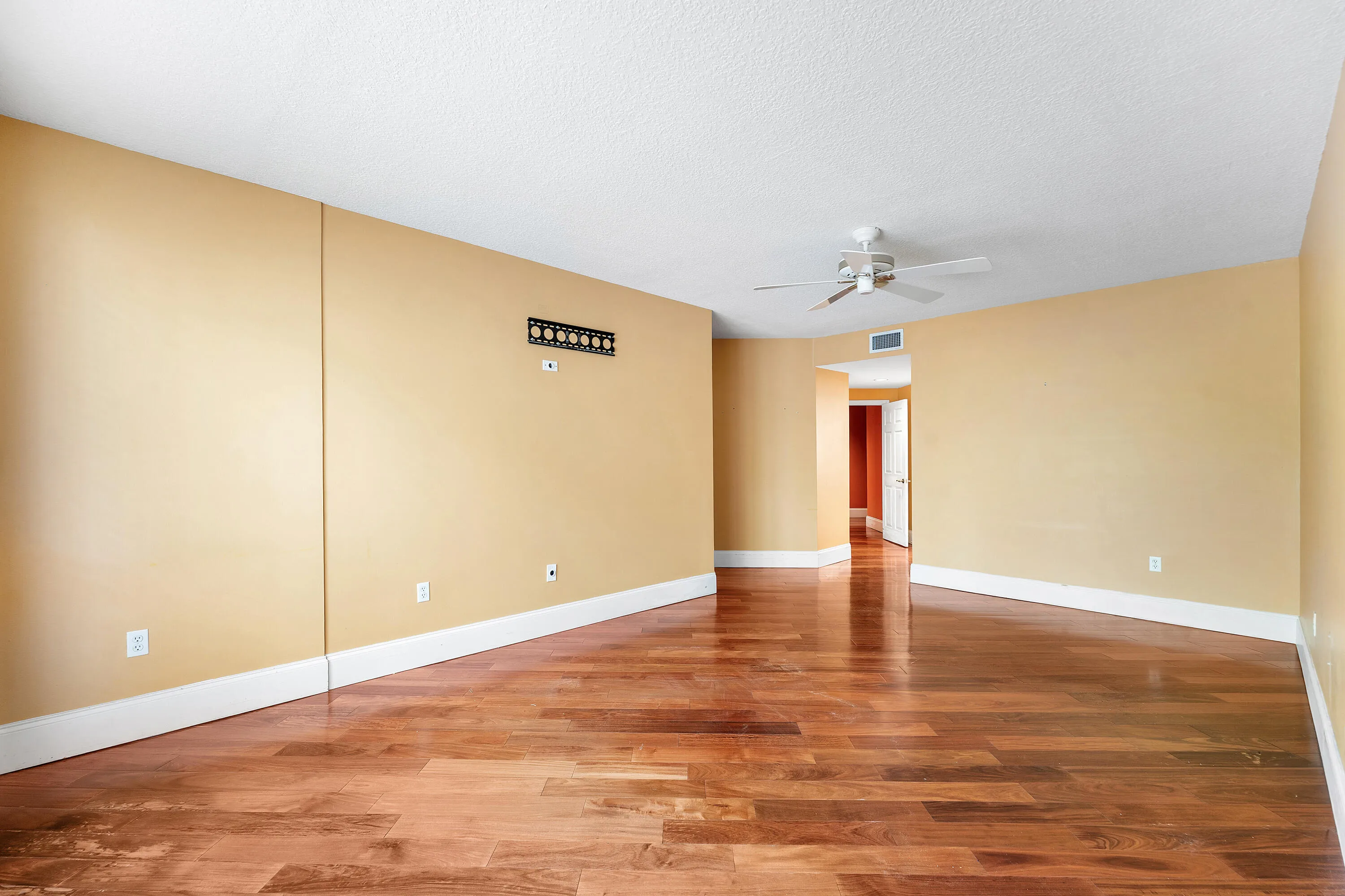 Spacious room featuring wood-finish flooring, light-colored walls, white baseboards, and a ceiling fan