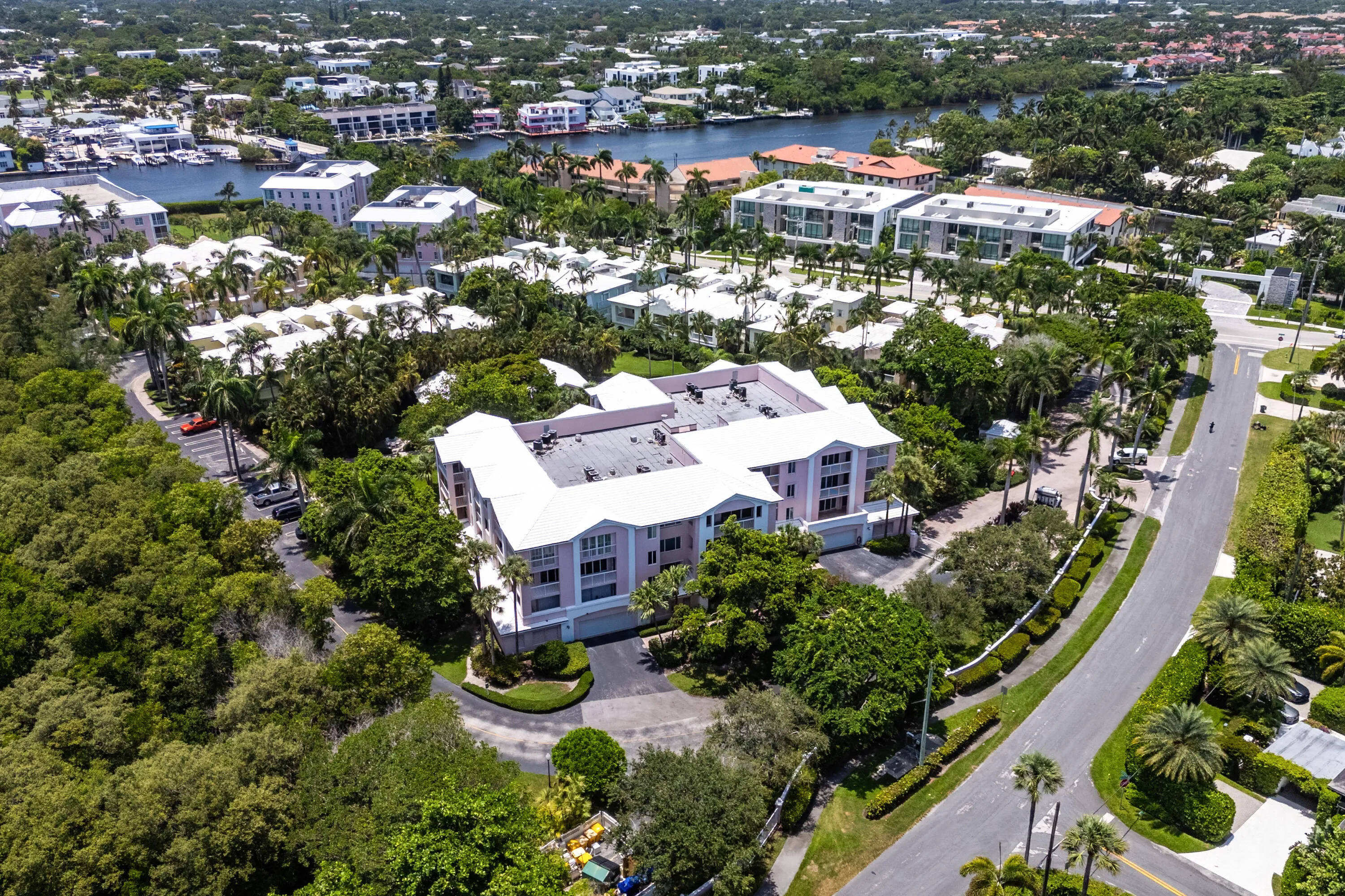 Multi-story residential building with a white roof and pale pink exterior, surrounded by lush green landscaping