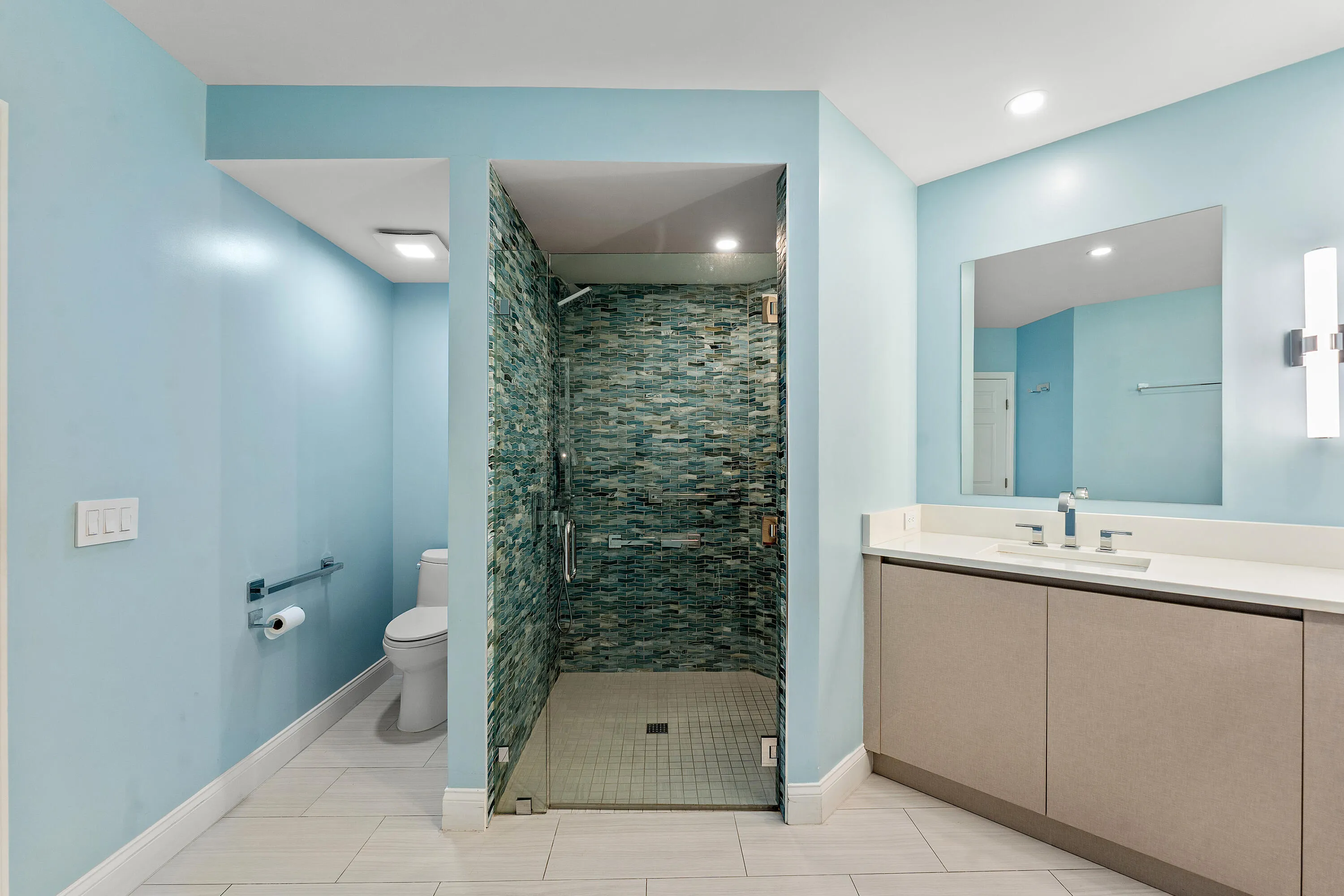 Bathroom featuring a glass-enclosed shower with mosaic tile surround, a single vanity with a quartz countertop, and a separate toilet area