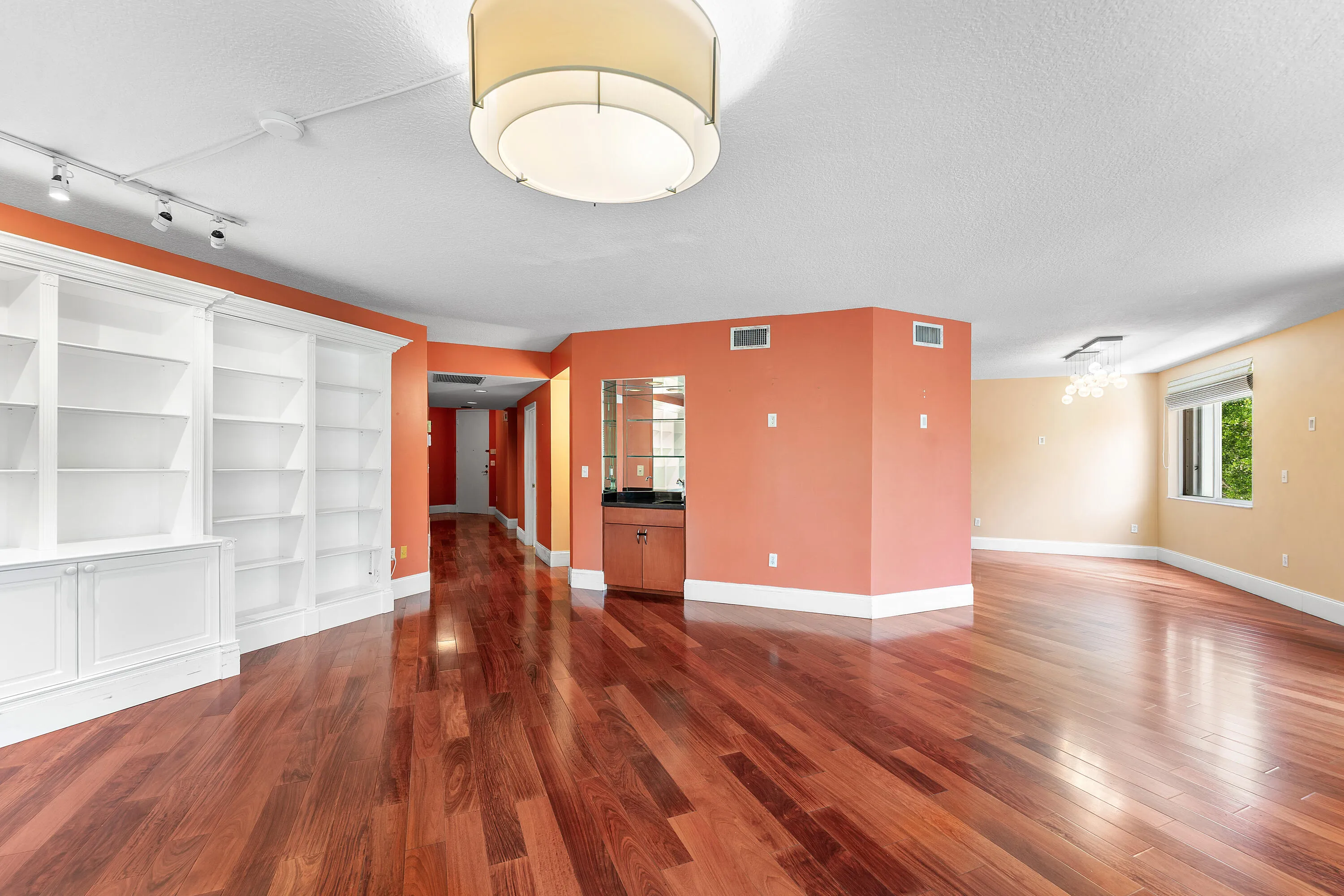 Spacious interior featuring wood-finish flooring, built-in shelving, a wet bar with a dark countertop and wood cabinetry, and multiple windows