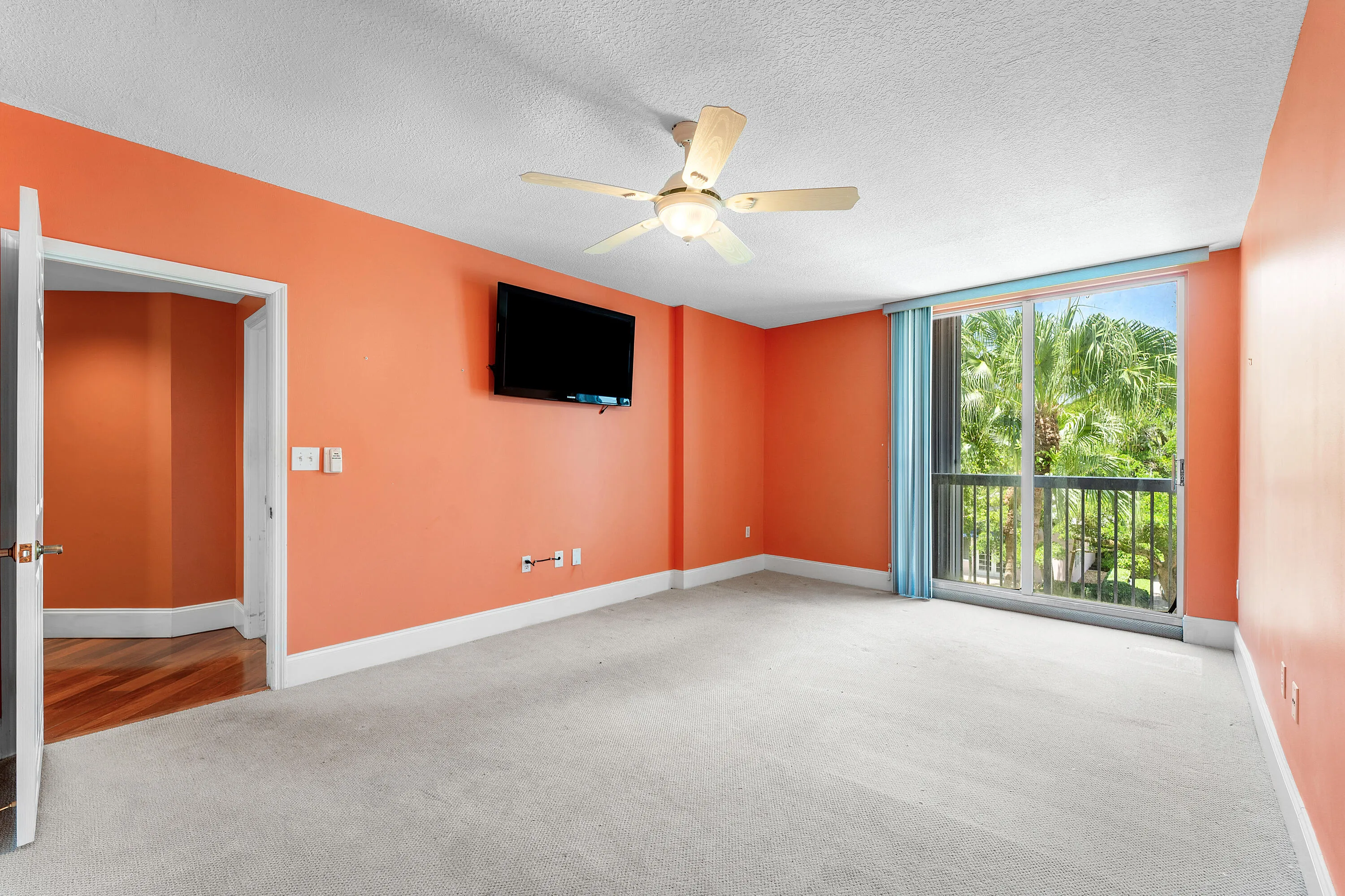Spacious room featuring a ceiling fan, carpeted flooring, and vibrant orange walls